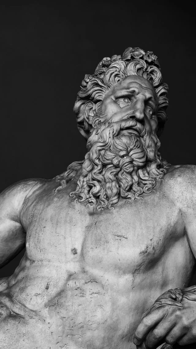 Black and white image of a marble statue of a man with curly hair and a long, curly beard. Photo by Pegah Sharifi courtesy of Pexels.