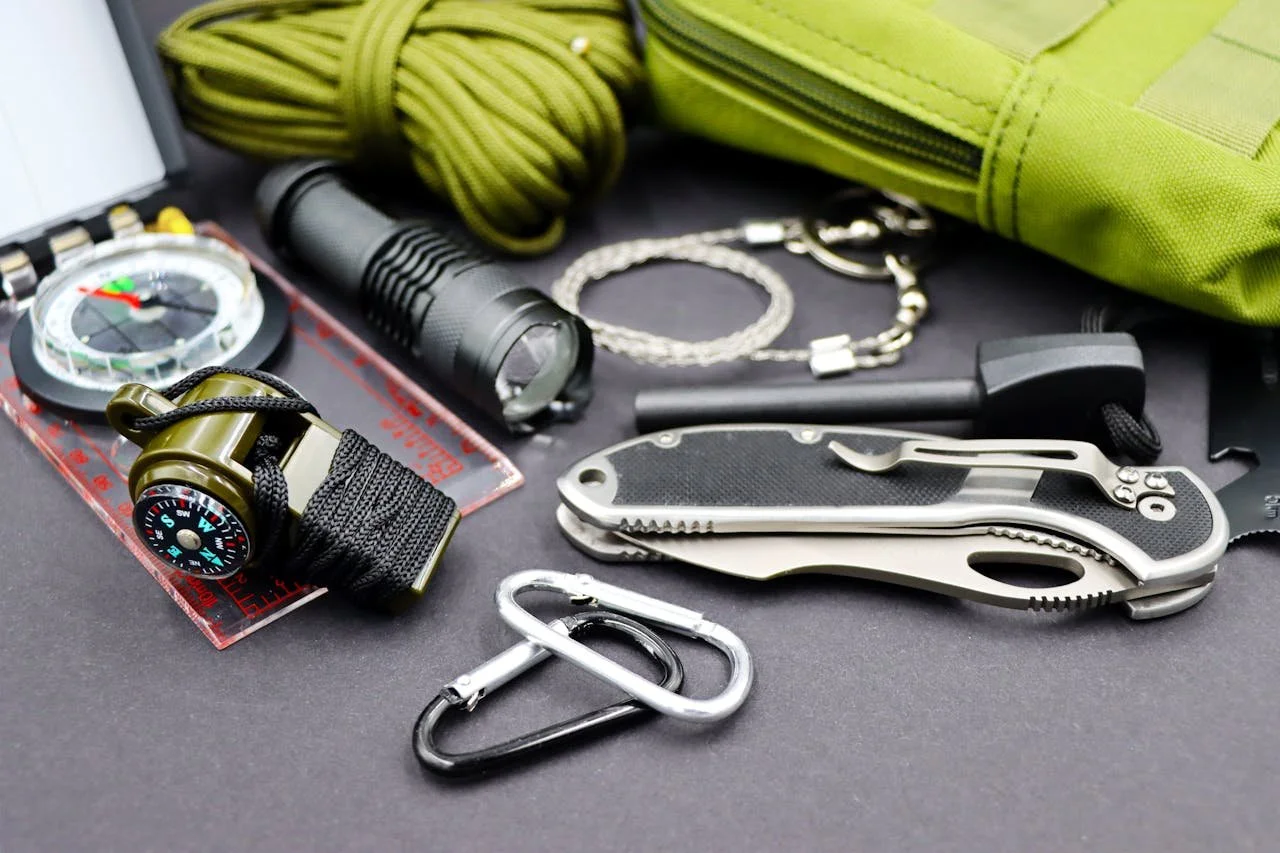 Survival gear on a table including a knife, flashlight, compass, whistle, fire-starting rod, and cord. Photo by Marta Branco.