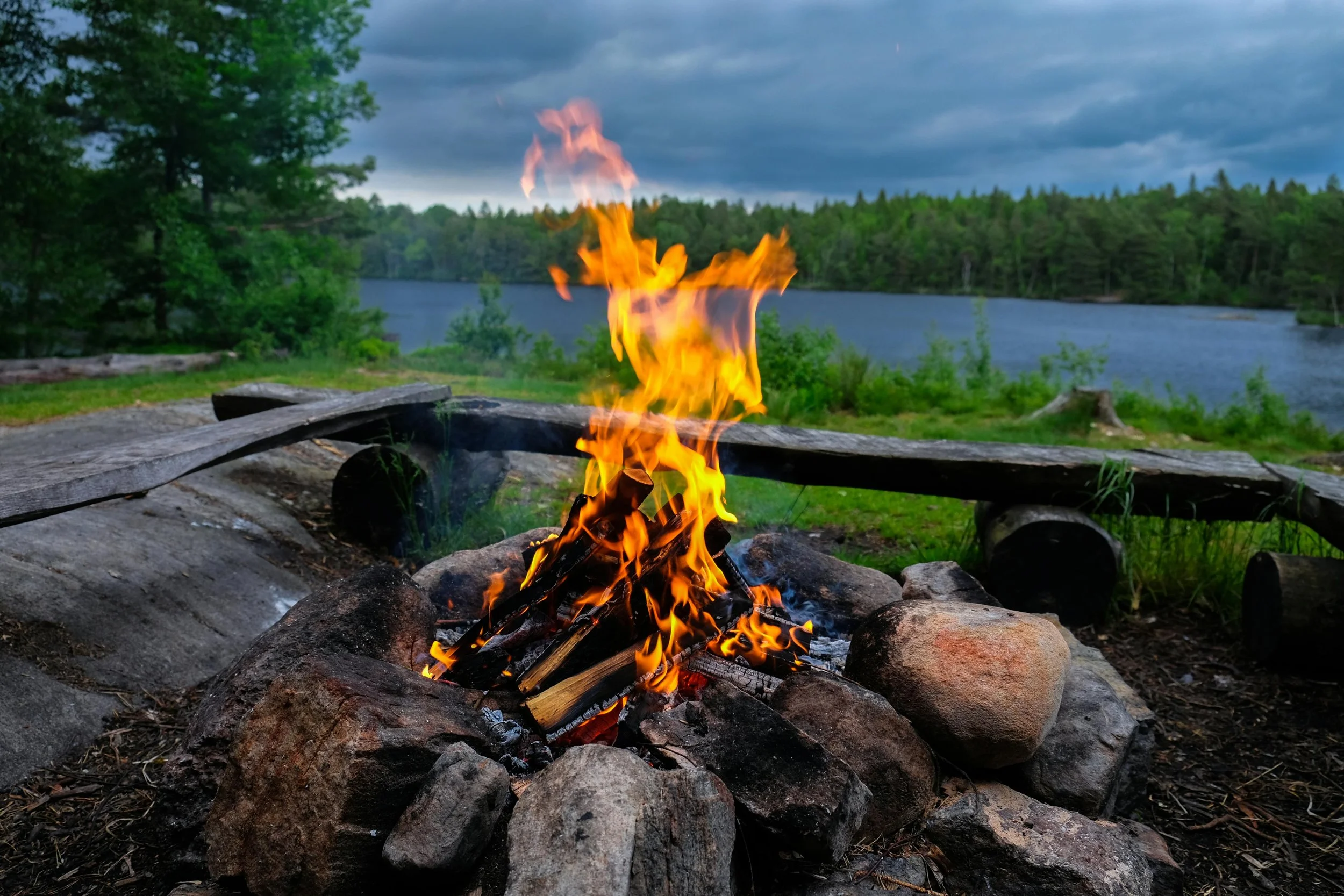 Campfire set in a circle of stones with benches around it near a lake