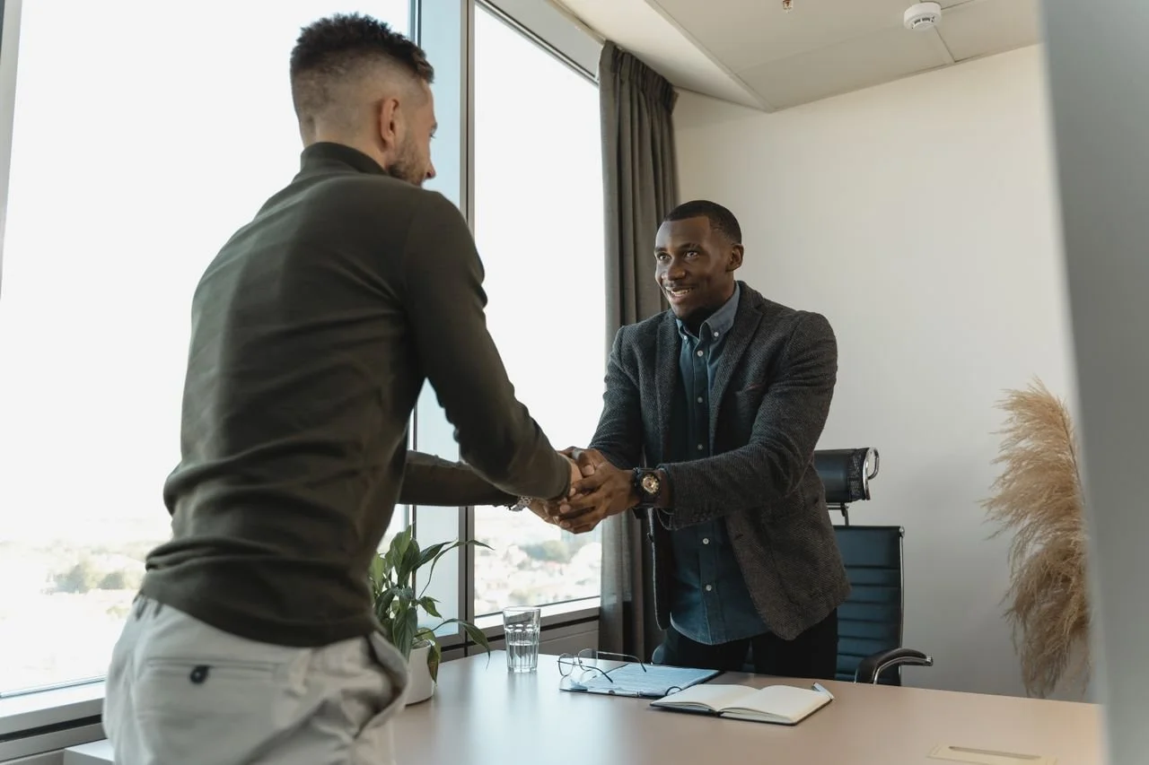 Man in turtleneck shirt shakes hands another man in a blazer. Photo by Tima Miroshnichenko courtesy of Pexels.