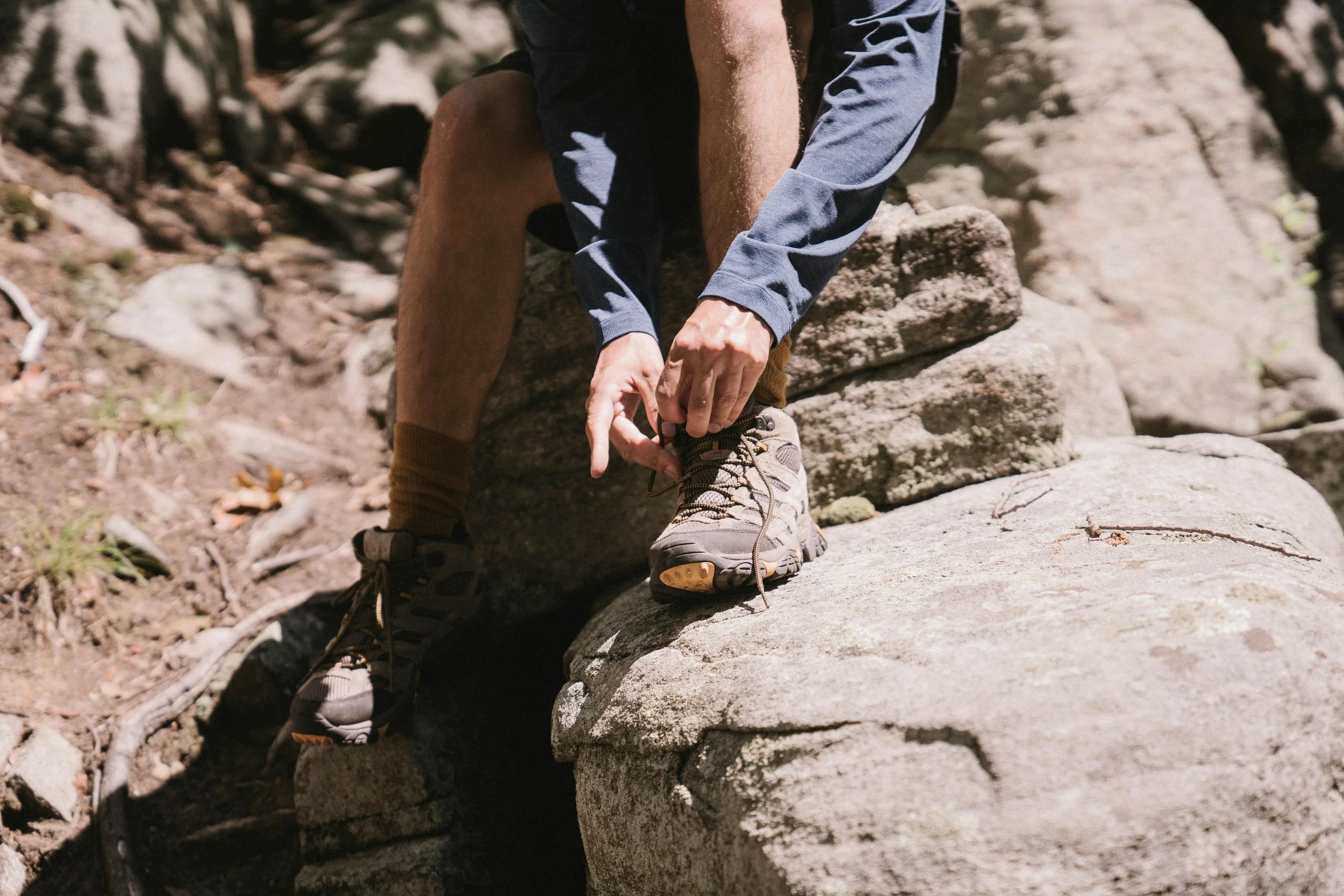 A man's hands seen lacing up his hiking boots while he sits on a rock.