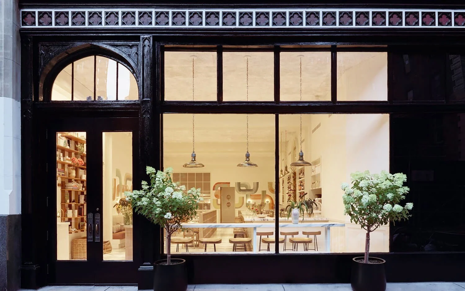 Elegant storefront with illuminated interior and lush potted plants | The Morris Project