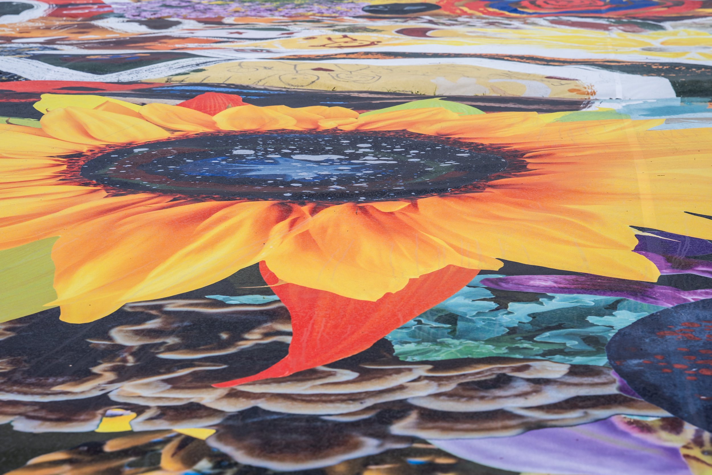 Close-up of a colorful floral mural featuring a large sunflower with bright yellow petals and a dark center, with abstract and vibrant background elements.