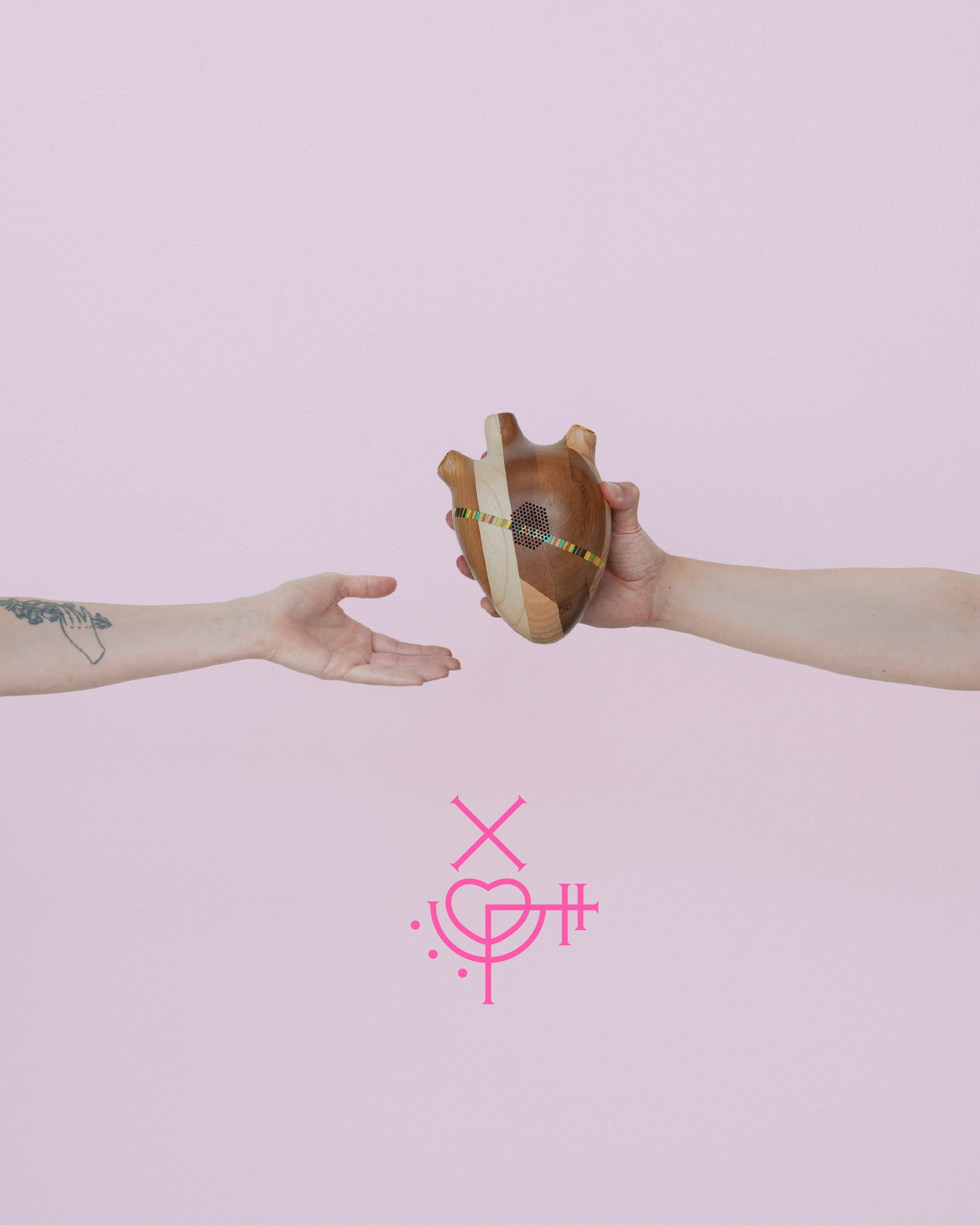 Two arms reaching towards each other, one holding a wooden, heart-shaped object with colorful band, pink symbols and dots below on a light pink background.
