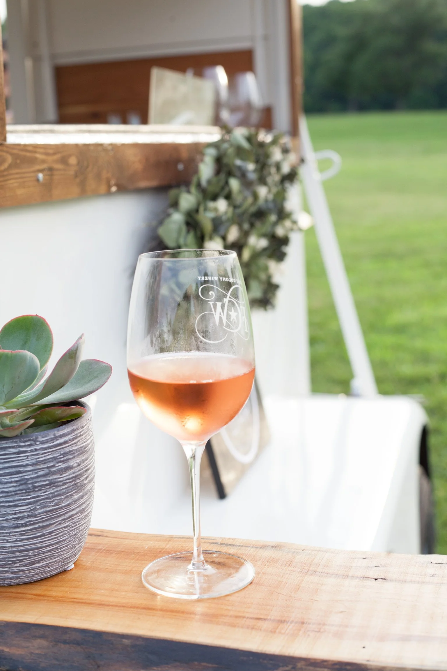 A glass of rosé wine on a wooden bar ledge with The Bitty Bar mobile bar in the background.