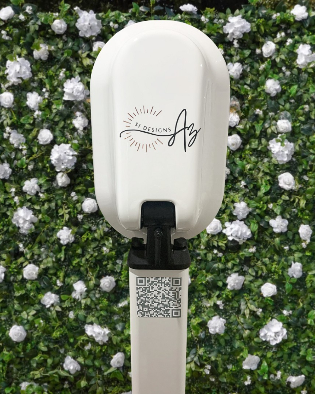 hand sanitizing station with logo for SI Designs AZ against a green leafy background with white flowers and a QR code.