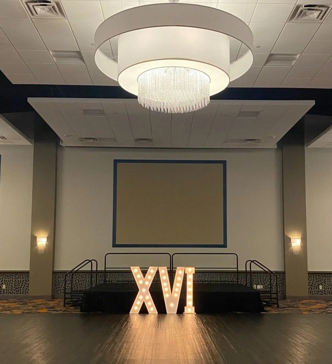Decorative illuminated Roman numeral 'XV' on a stage in a banquet hall.