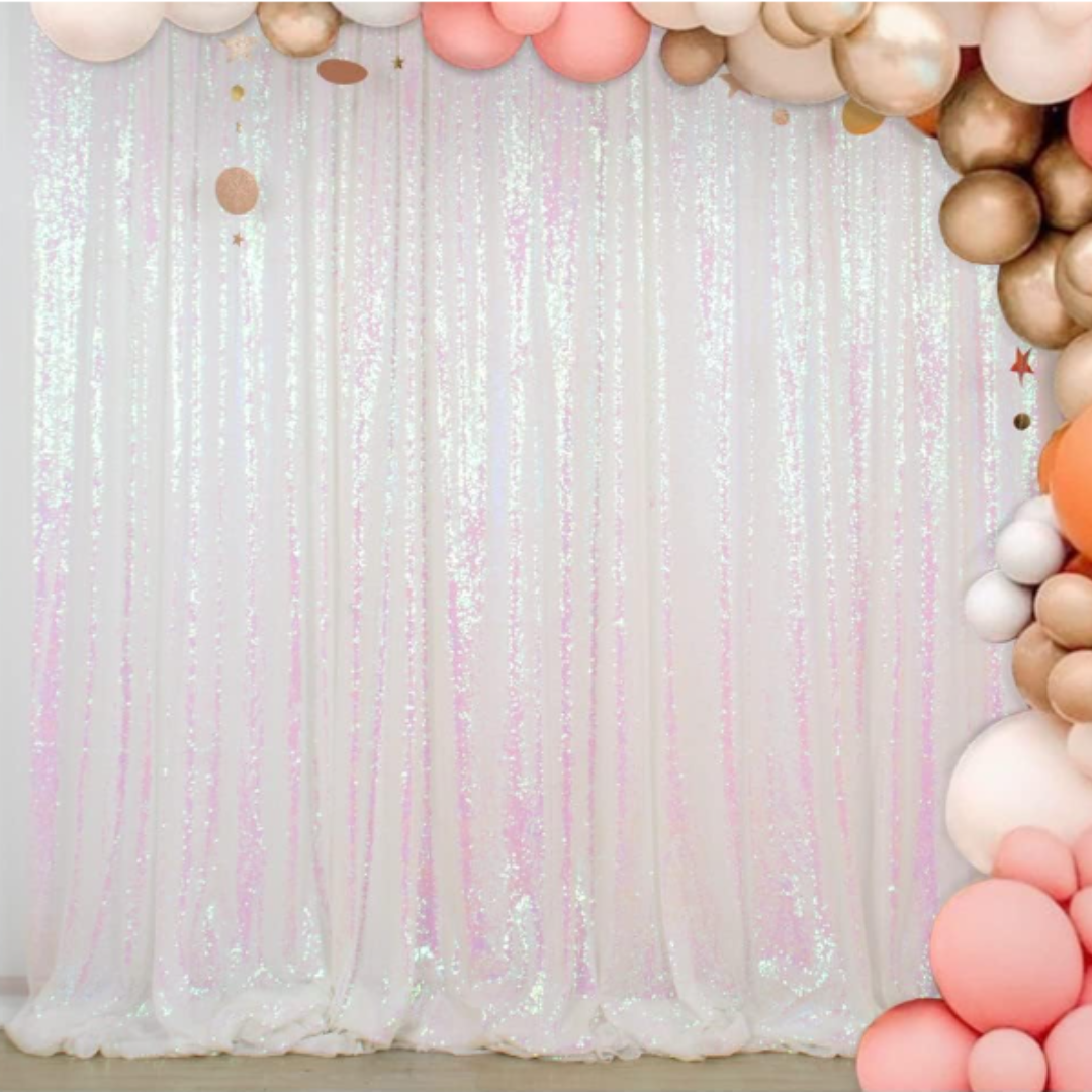 Decorative backdrop with iridescent vertical streamers and a balloon arch made of pink, white, beige, peach, and gold balloons, with small star-shaped ornaments.