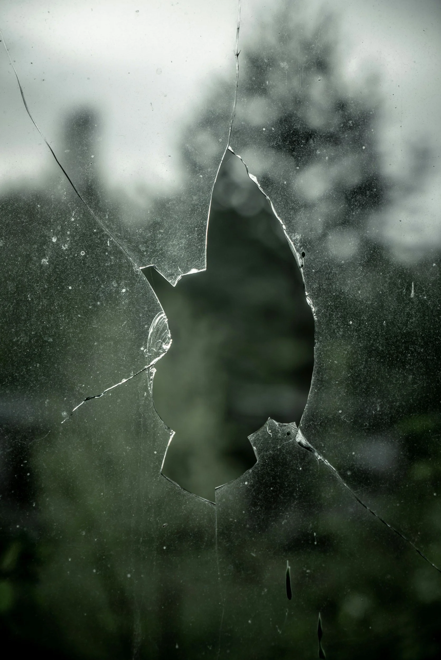 Close-up of a broken and cracked glass window with a blurry outdoor background.