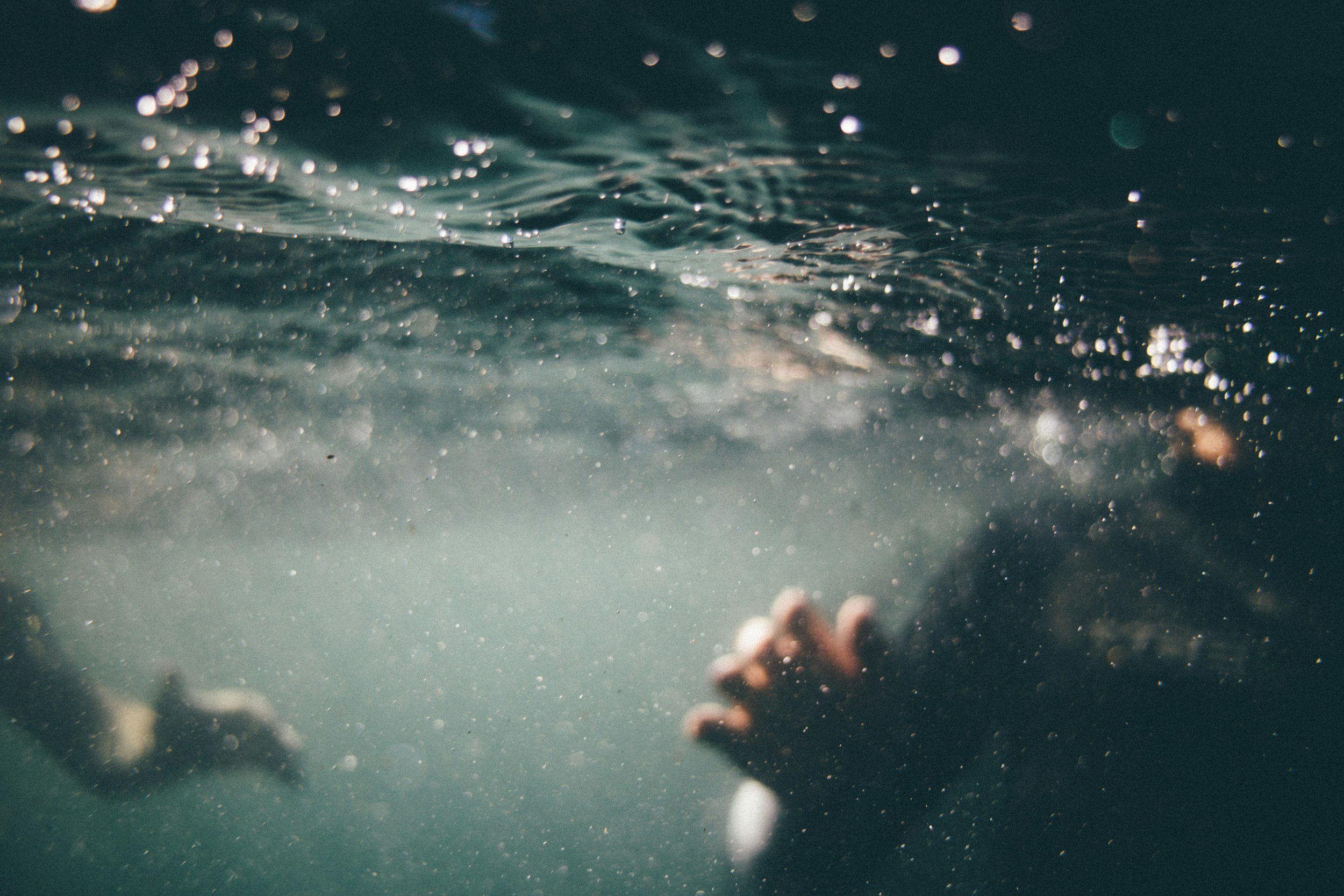 Underwater view of the ocean with bubbles and waves, blurry shape of a person holding an object in the foreground.