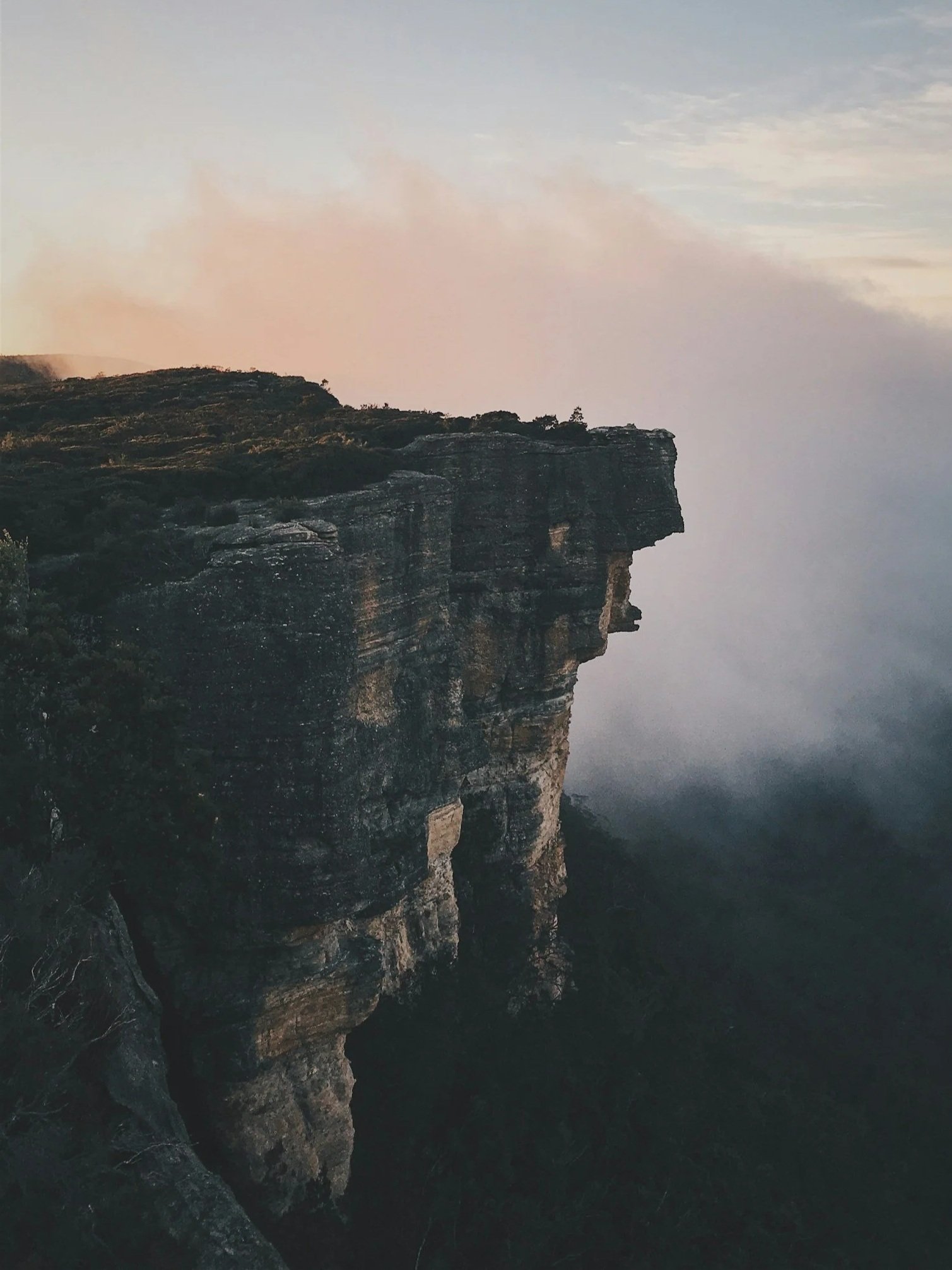 Cliffside overlooking a foggy or misty landscape with a cloudy sky.