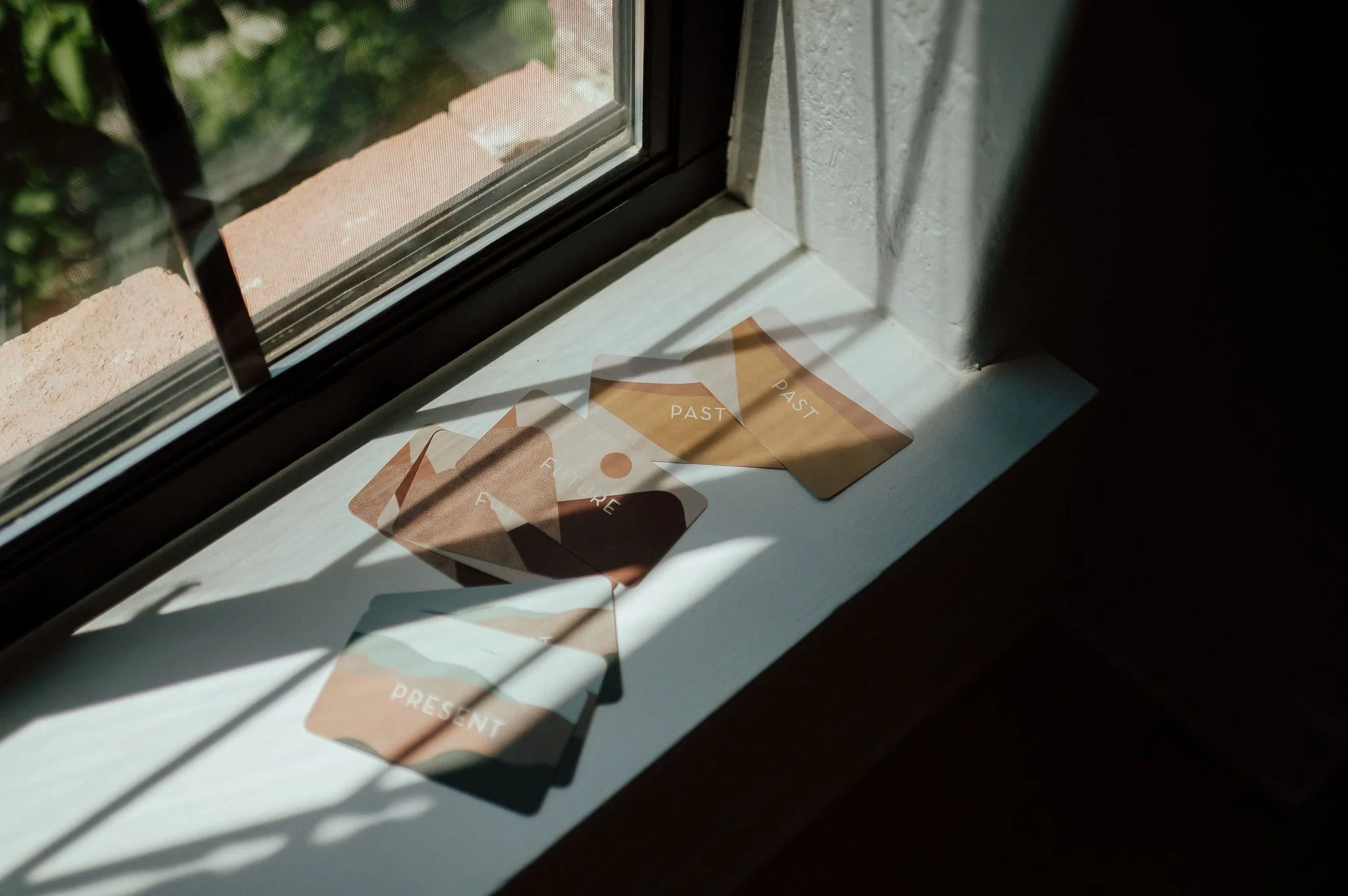 Sunlight casts shadows on a windowsill. There are cards labeled 'PAST,' 'PRESENT,' and 'FUTURE' on the windowsill.