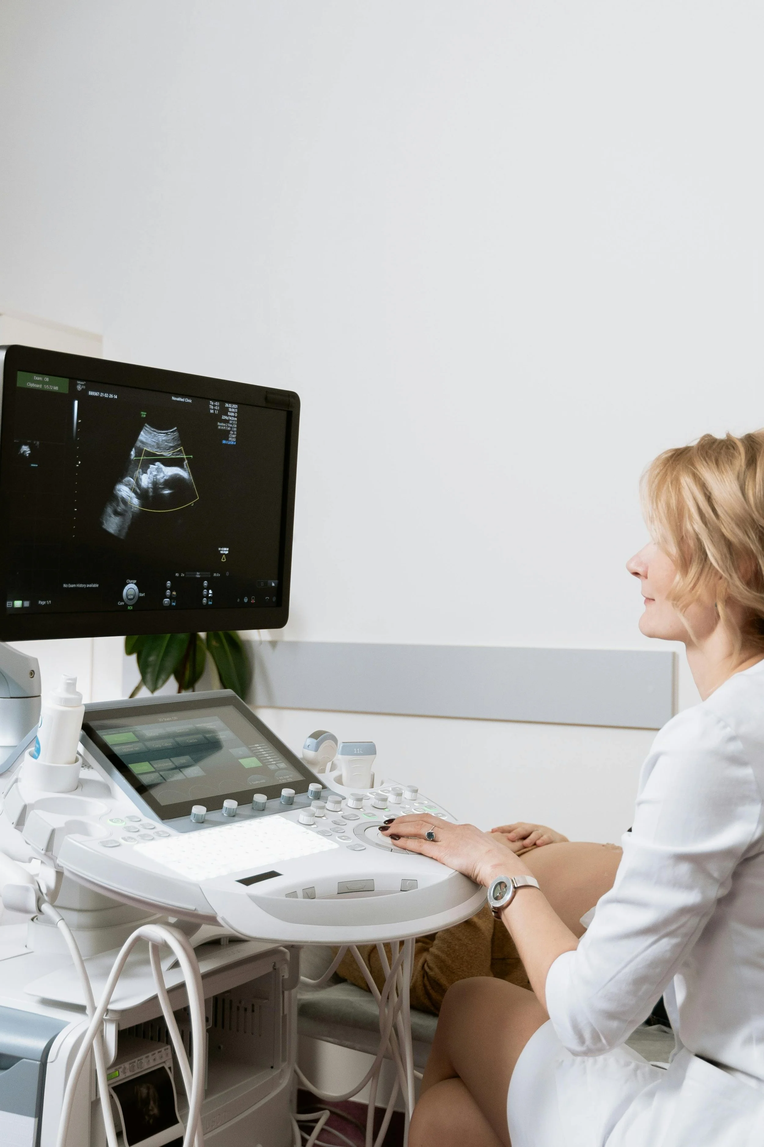 A woman sitting on an examination table during an ultrasound, viewing the fetus on a monitor in a medical clinic.