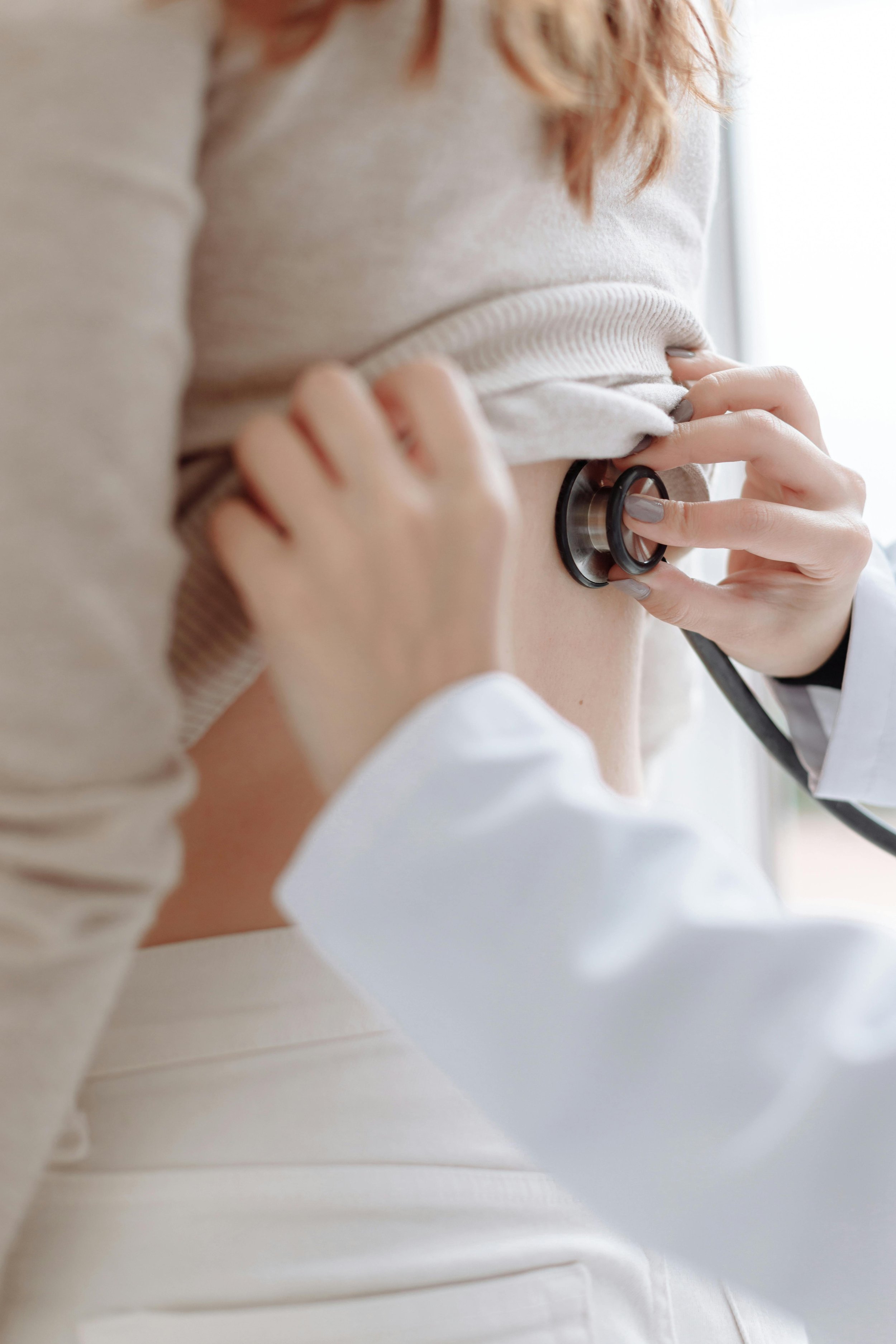 Medical professional uses stethoscope to examine a woman's back while she lifts her shirt.