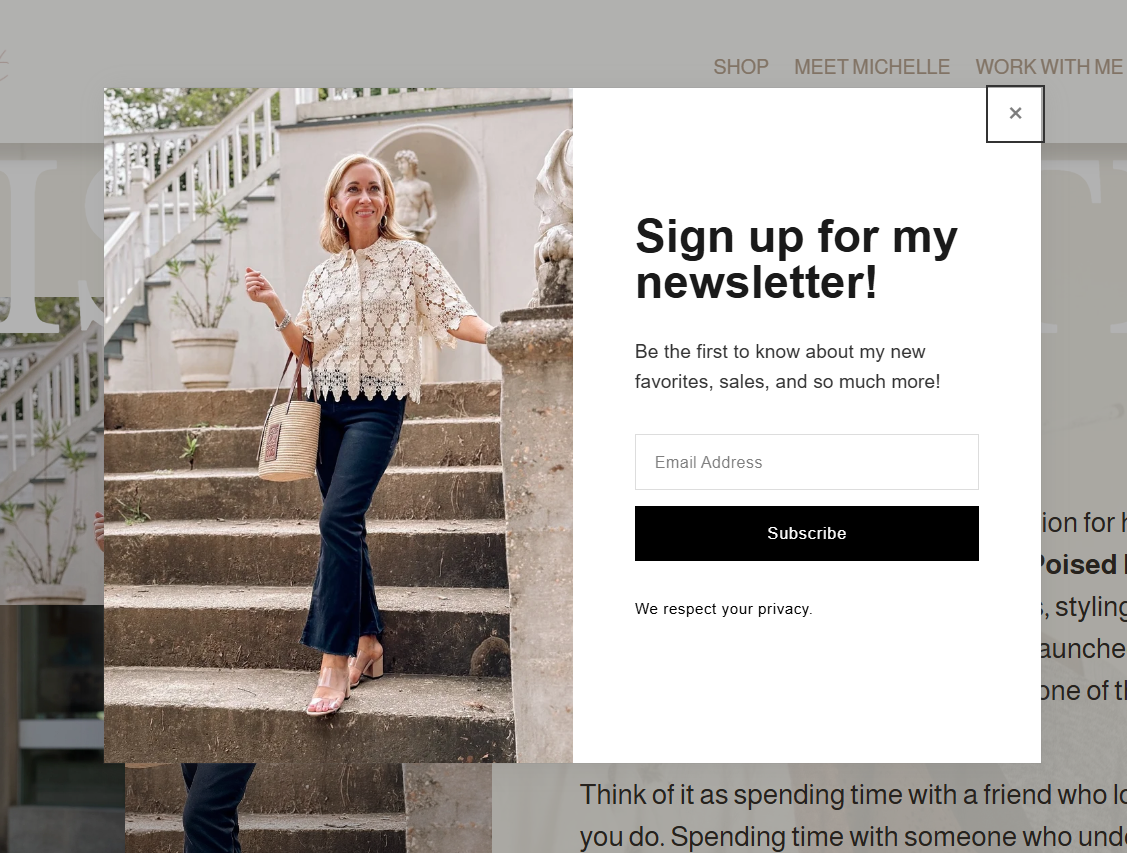 A woman sitting on outdoor stairs, smiling, wearing a lacy white top and dark pants, holding a woven handbag.
