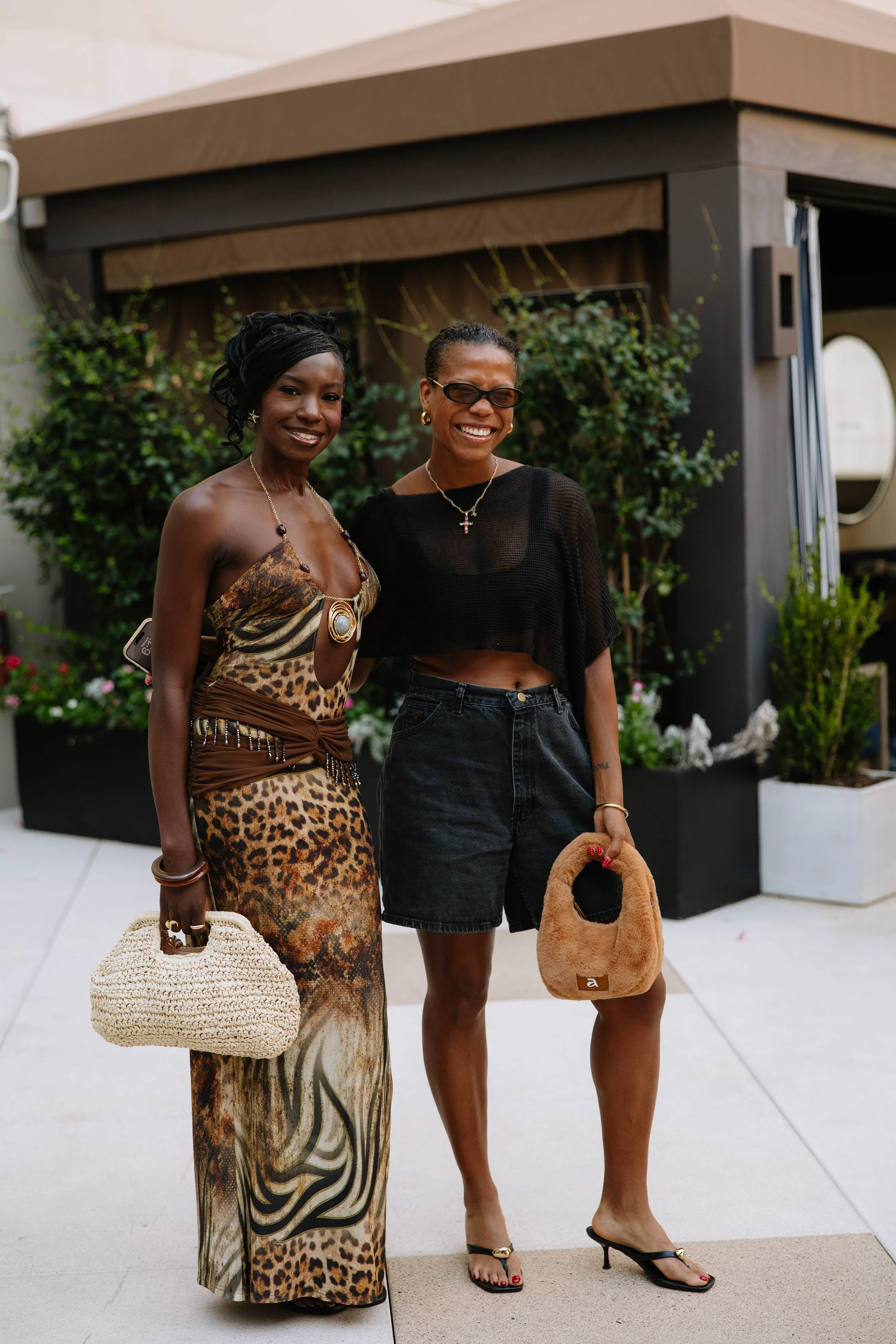 Two girls wearing matching sets one with a black shirt and shorts and the other with an animal print shirt and skirt. Both have neutral handbags.