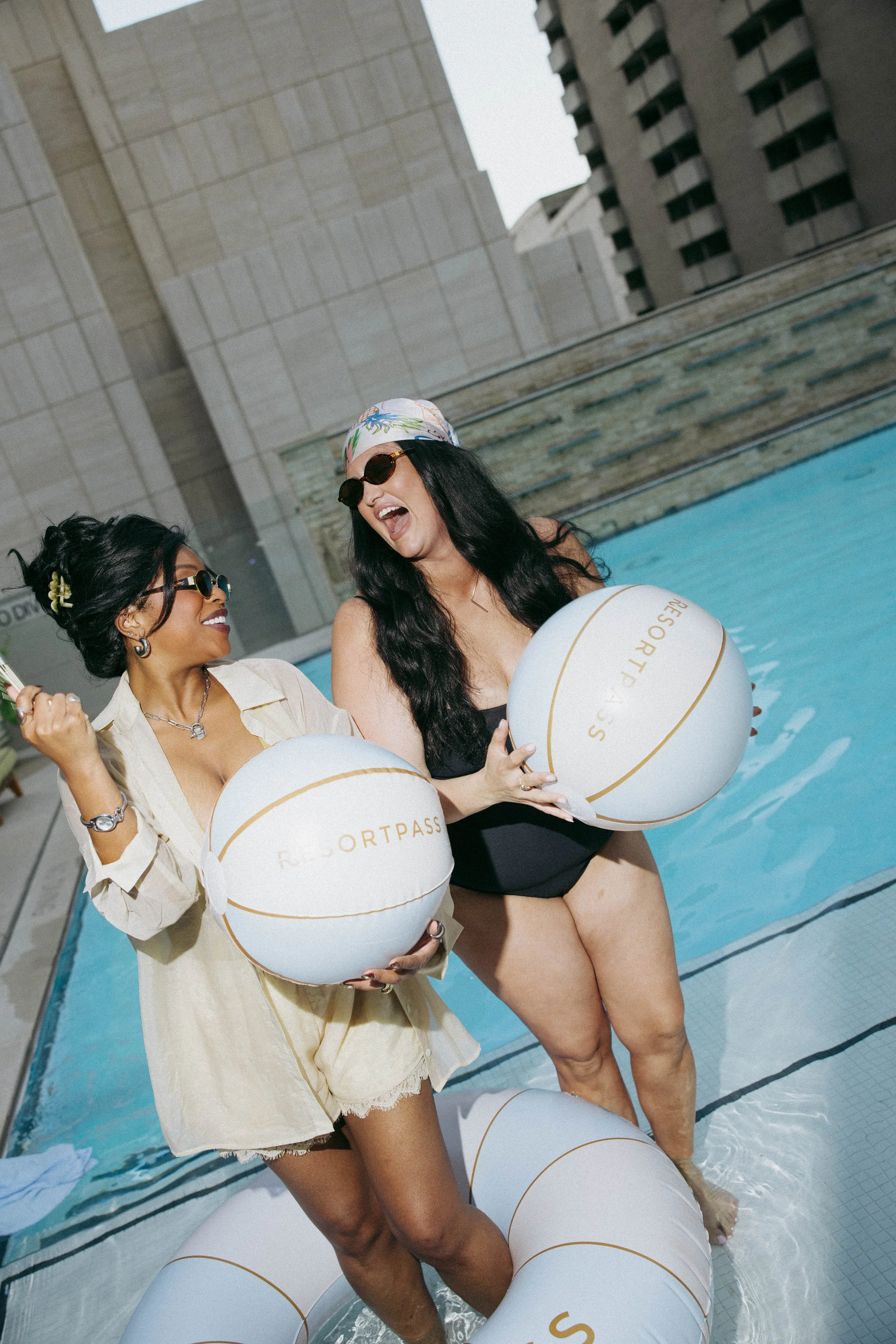 Influencers smiling with custom beach balls in front of a luxury blue pool and candidly smiling.
