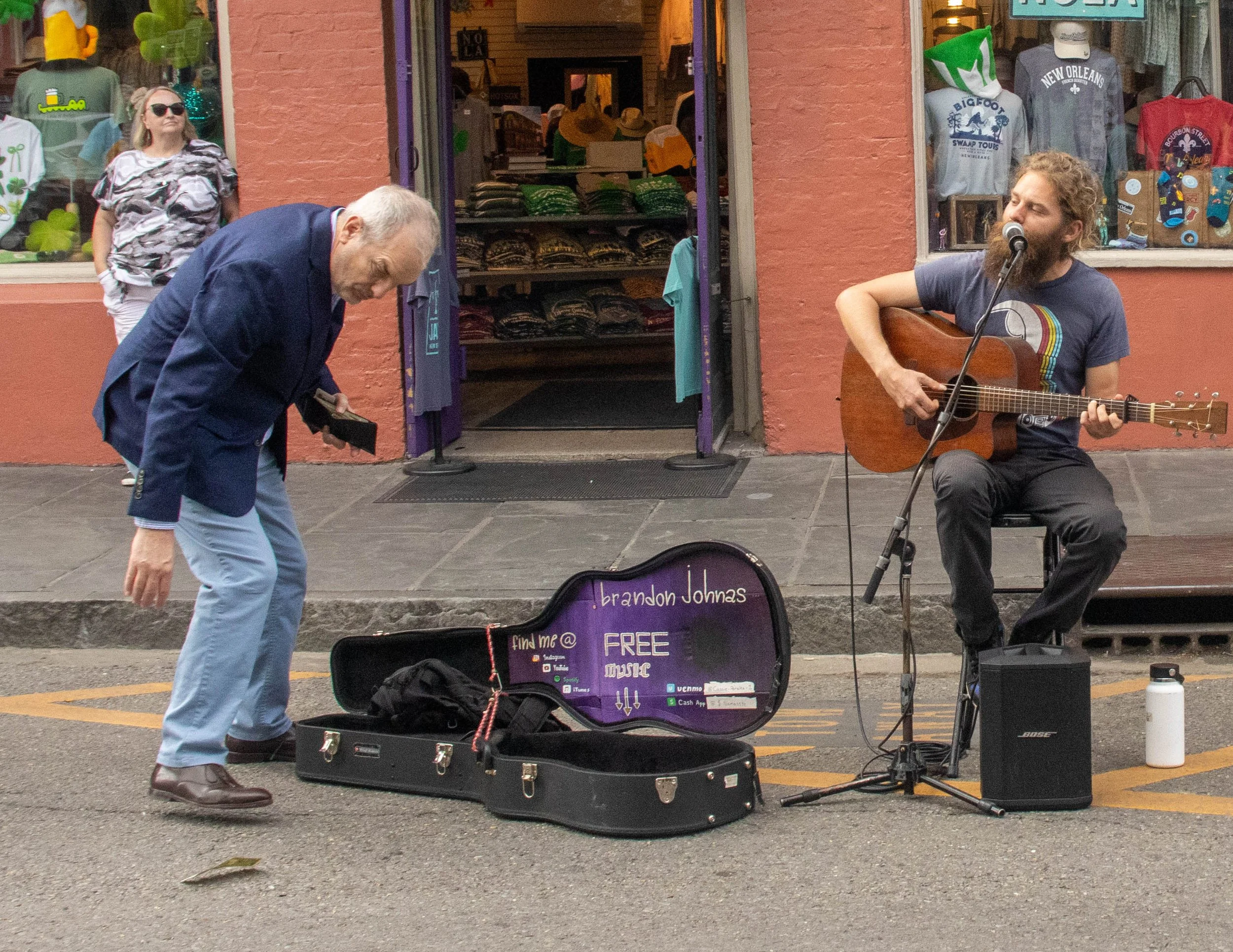 Brandon Johnas performs on Royal Street in the French Quarter in New Orleans on Sunday afternoon, March 15, 2026. Johnas watches as a man's tip flies away from his guitar case, repurposed as a tip jar.