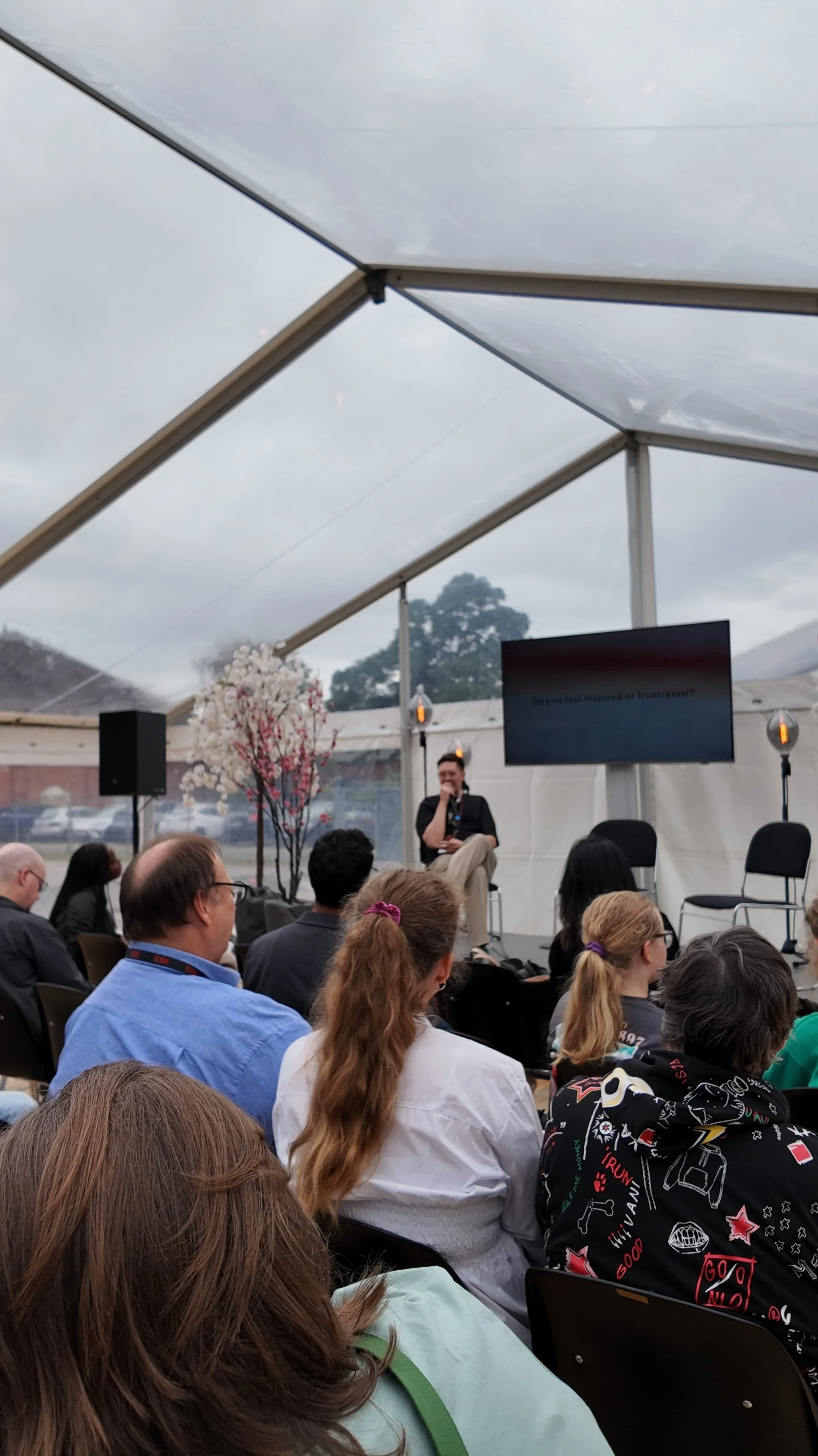 People attending a seminar under a transparent tent, with a speaker on stage and a screen displaying a question.