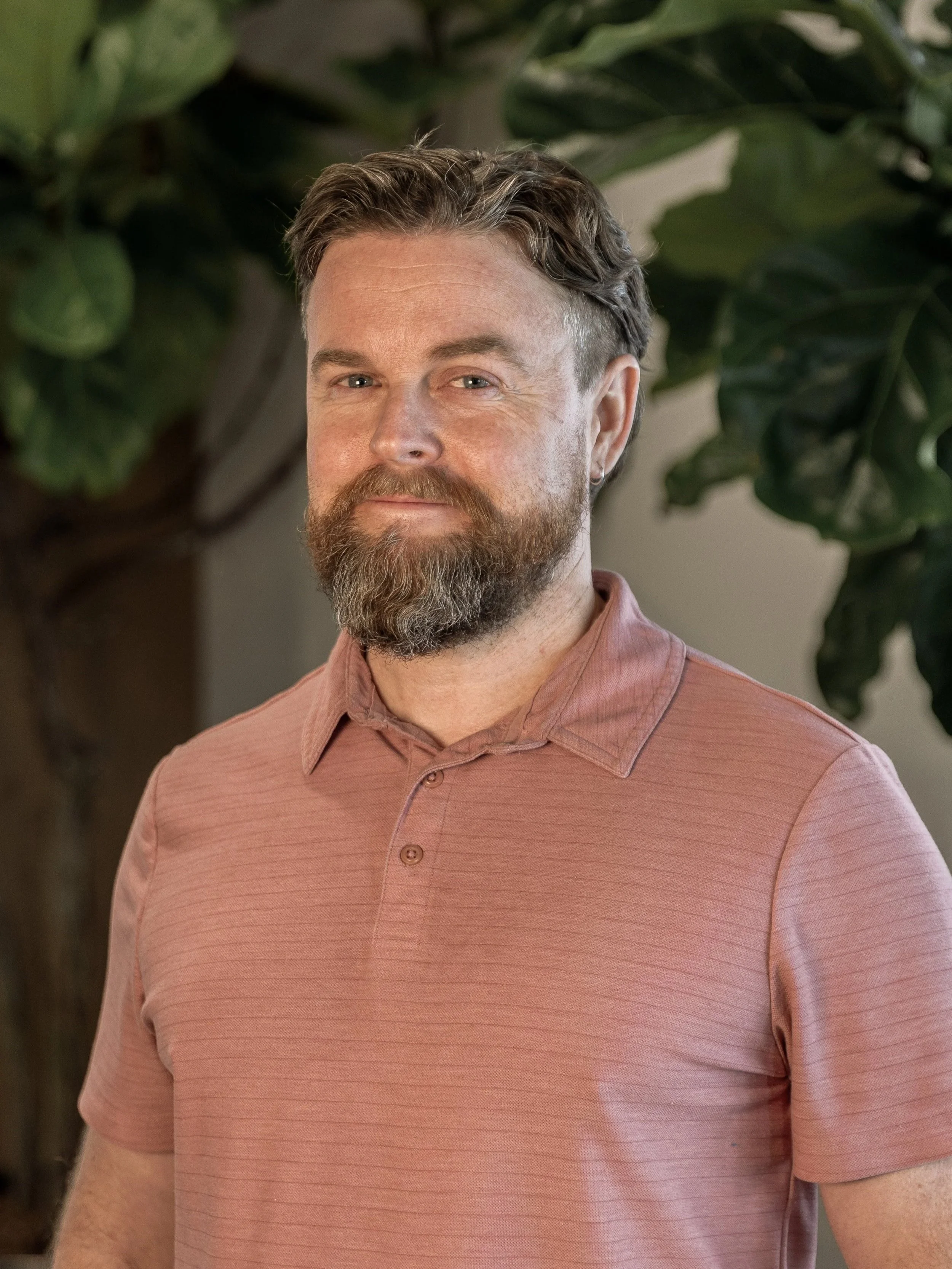 Man with neatly trimmed beard and brown hair, smiling in blue shirt.