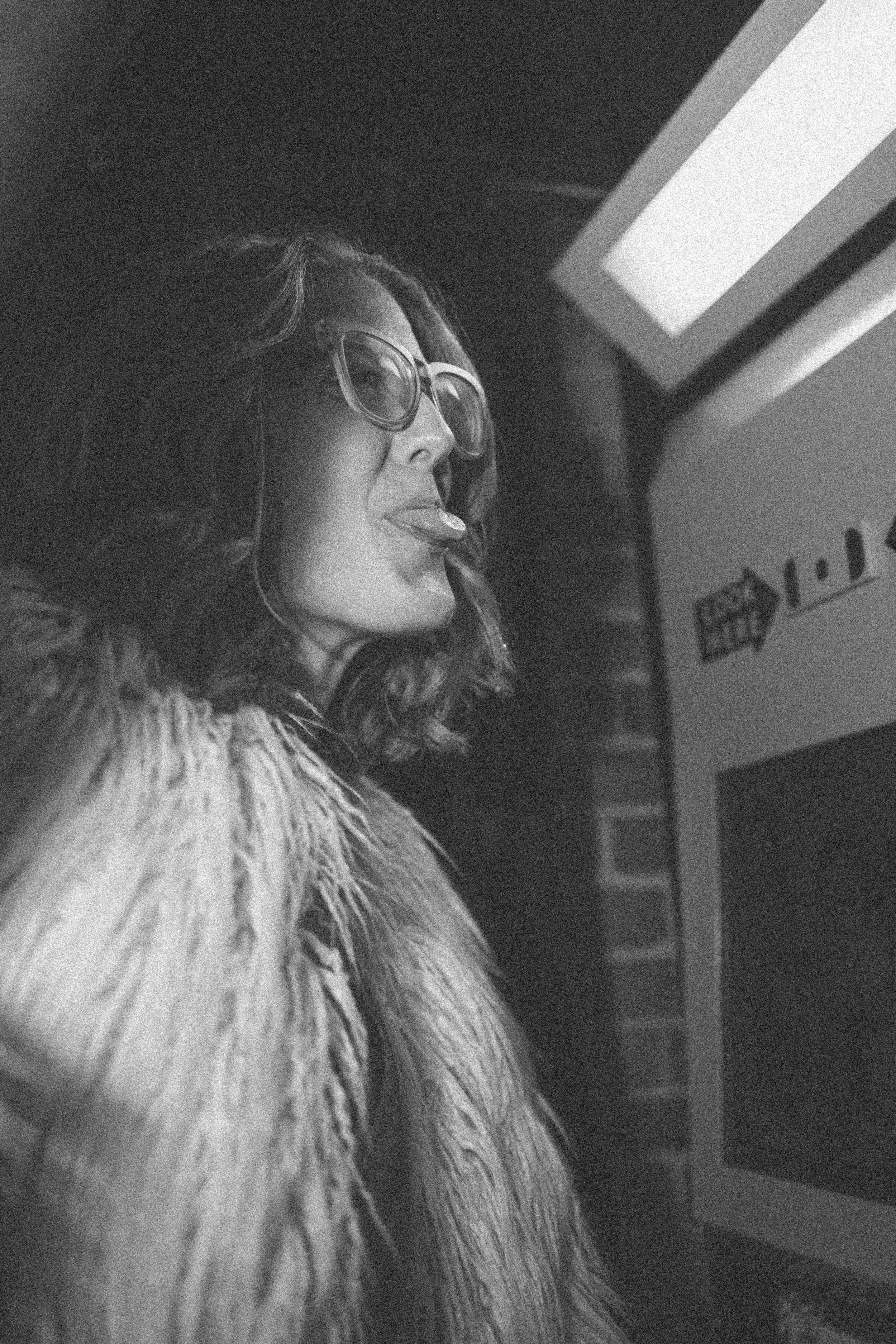 Woman with glasses sticking out her tongue while looking at a computer screen.