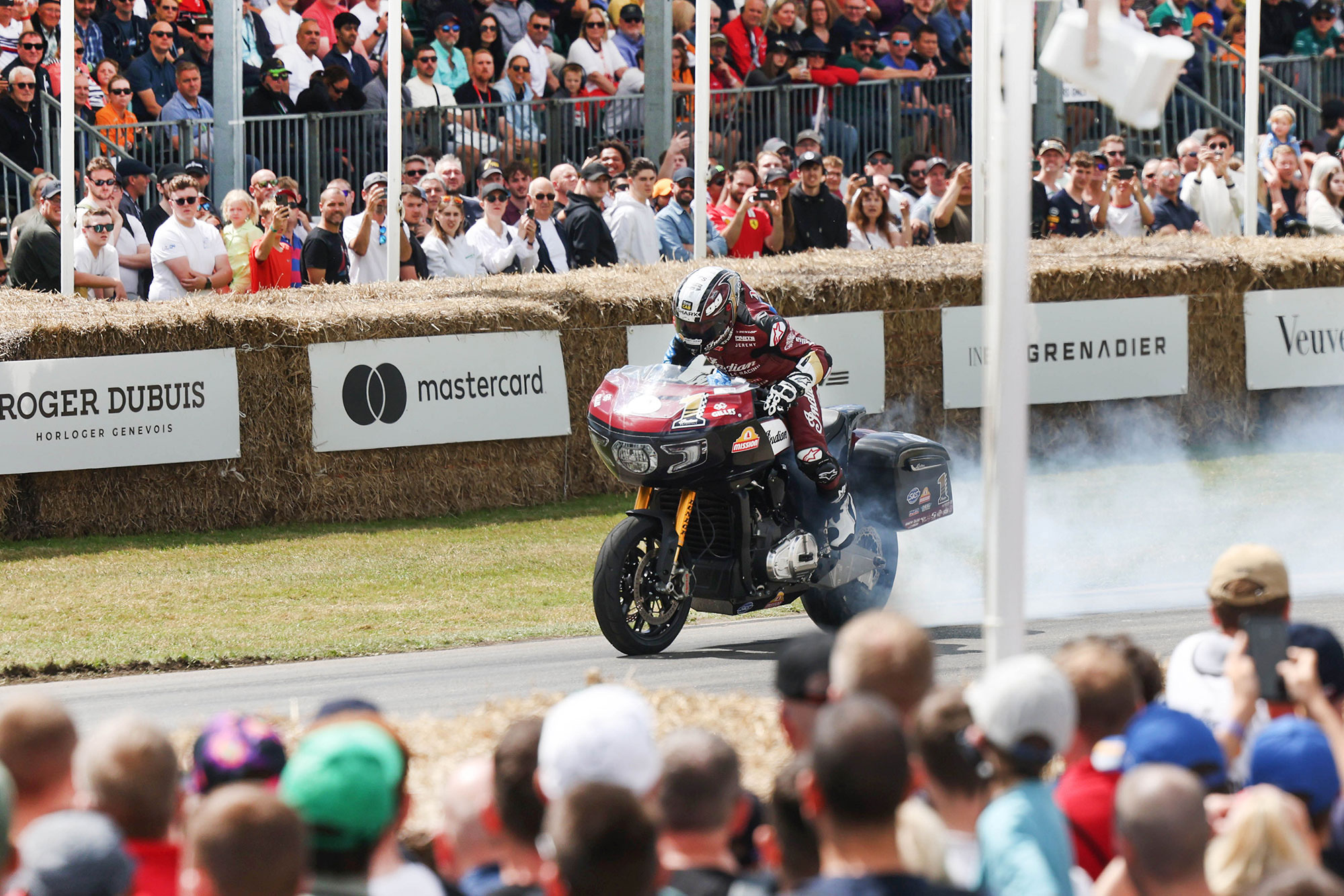 Motorcycle climbing the Goodwood hillclimb with hay bales and spectators lining the course