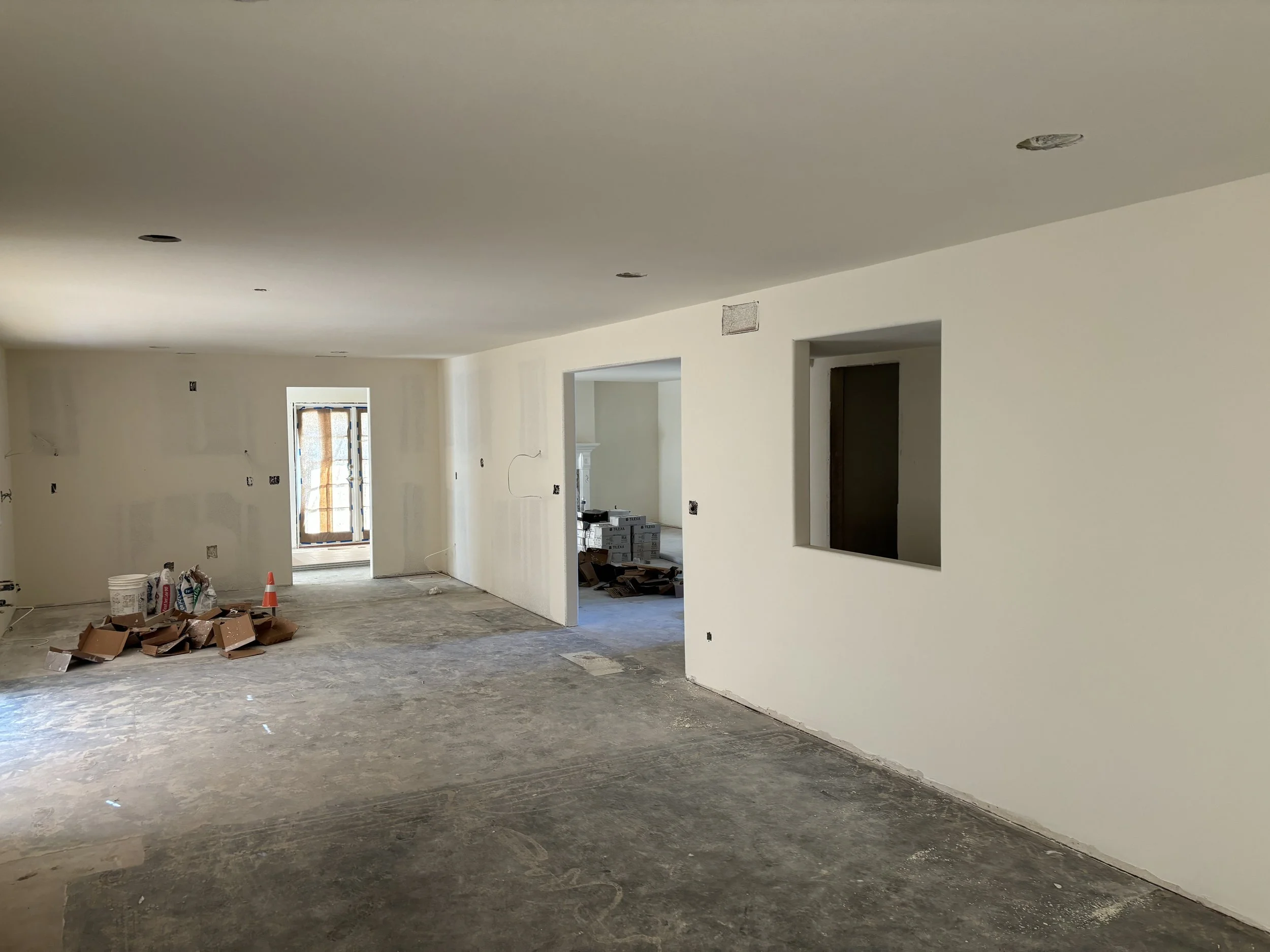 Interior of a room under construction with unfinished flooring, newly finished level 5 walls, and exposed electrical fixtures on the ceiling in Orange, California.