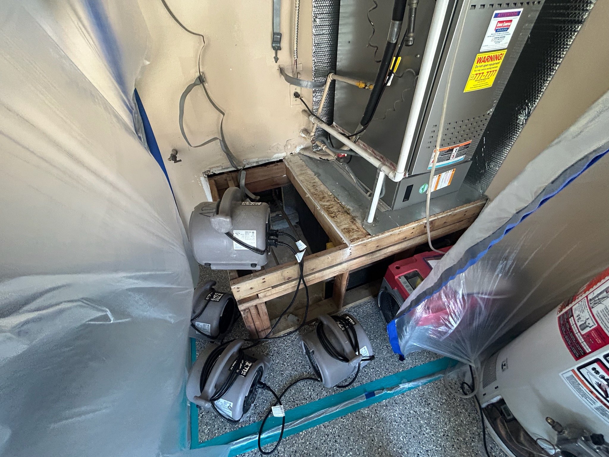 HVAC system being dried out after experiencing water damage with tools and equipment in a utility room, including a furnace, a portable heater, and various electrical components. The system is being dried out with fans.  