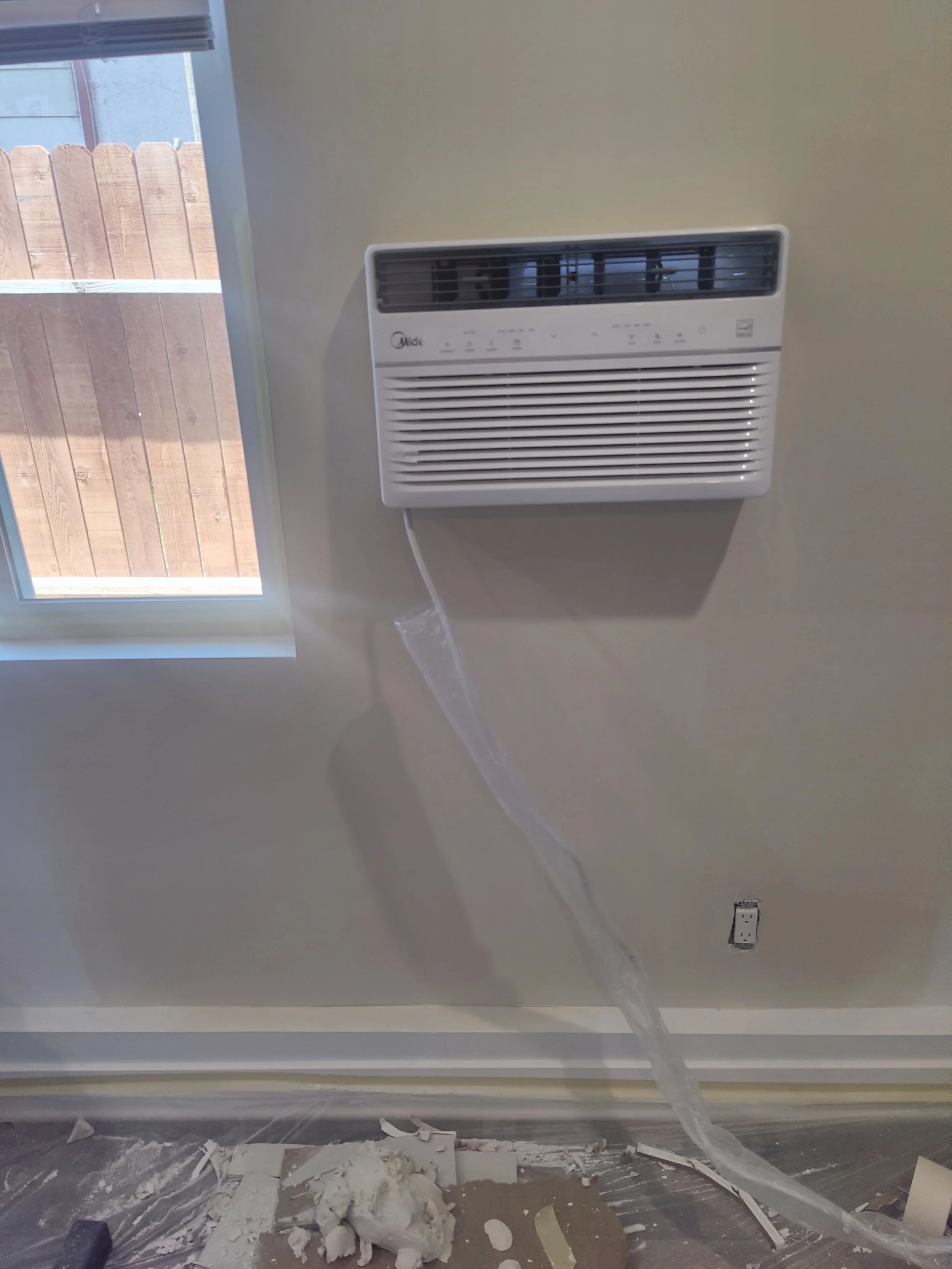 A seamless smooth texture drywall patch that is in the middle of being cleaned up. plastic of the floor, window, and AC to cover if from drywall compound, and keep the job site clean. 
