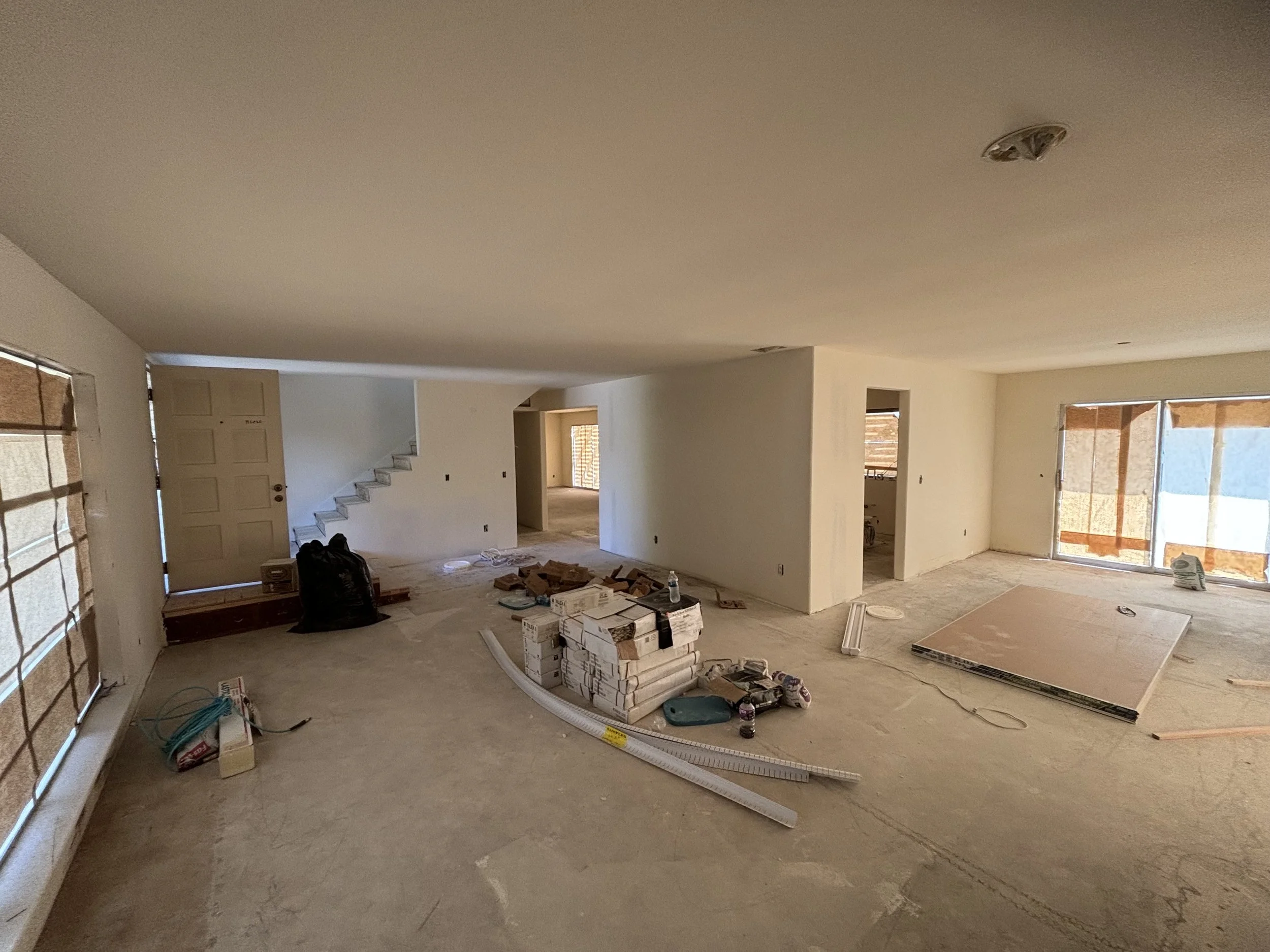 Interior of a house under construction with unfinished floors, construction materials, and partially covered windows.