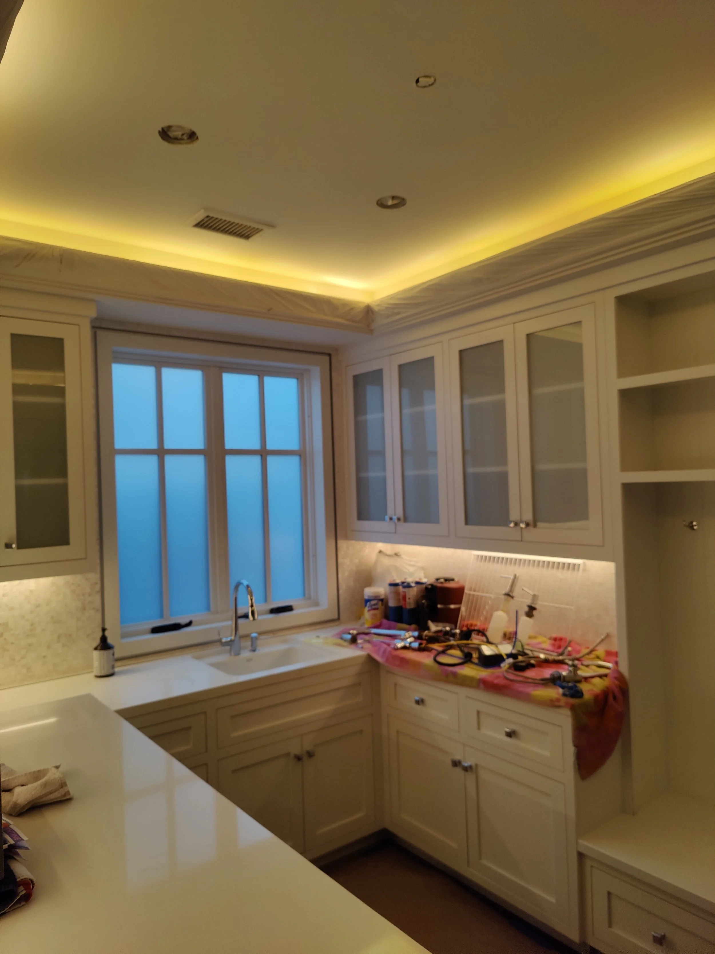Kitchen with white cabinets, a large window, and under-cabinet lighting. The countertop has tools and supplies, indicating ongoing renovation.