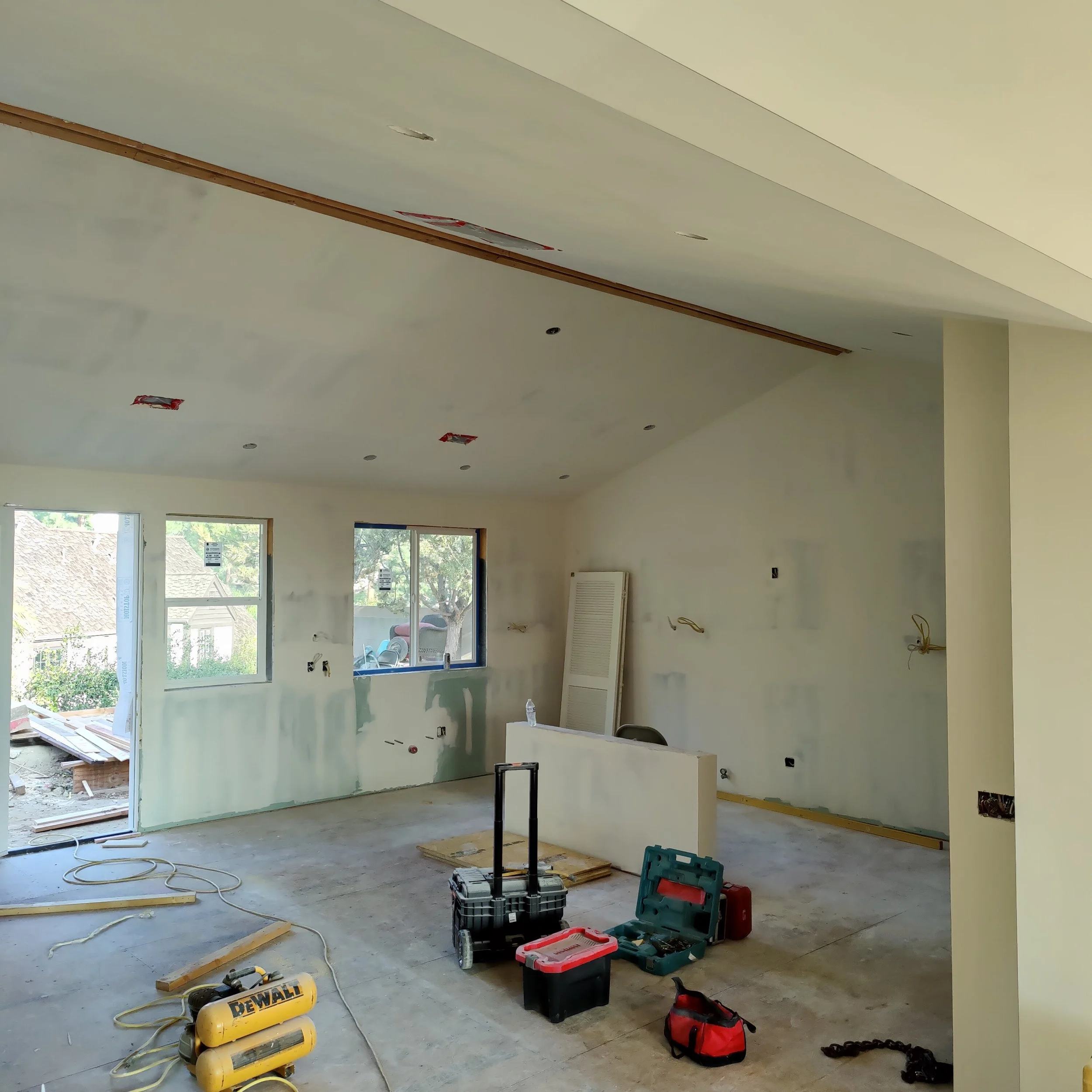 Room under construction with tools and equipment on the floor, unfinished drywall, and electrical wiring visible.