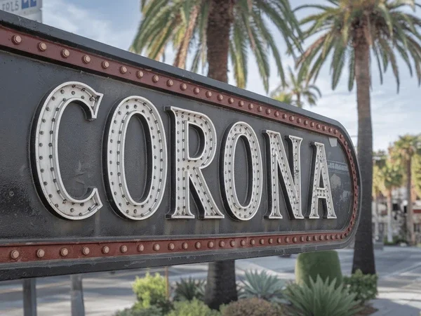 Close-up of a vintage-style sign with the word "Corona" on it, set against palm trees and a street scene in the background.