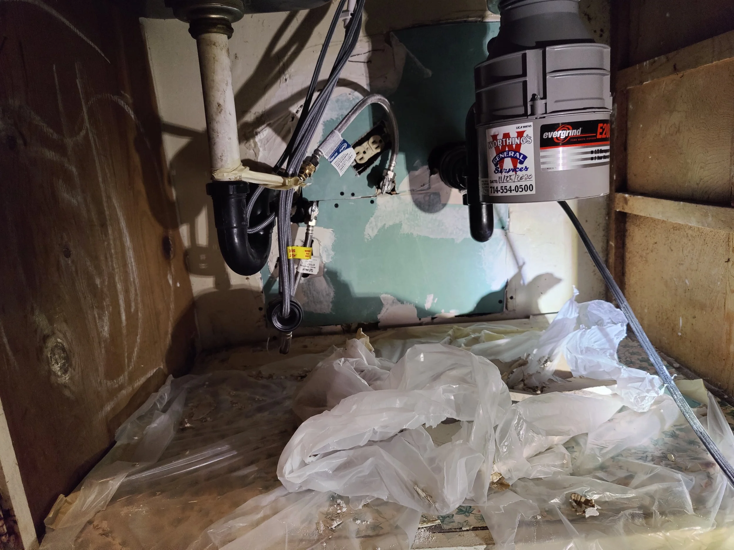 Installation of a sump pump system in a basement, with pipes, wiring, and plastic sheeting on the floor.