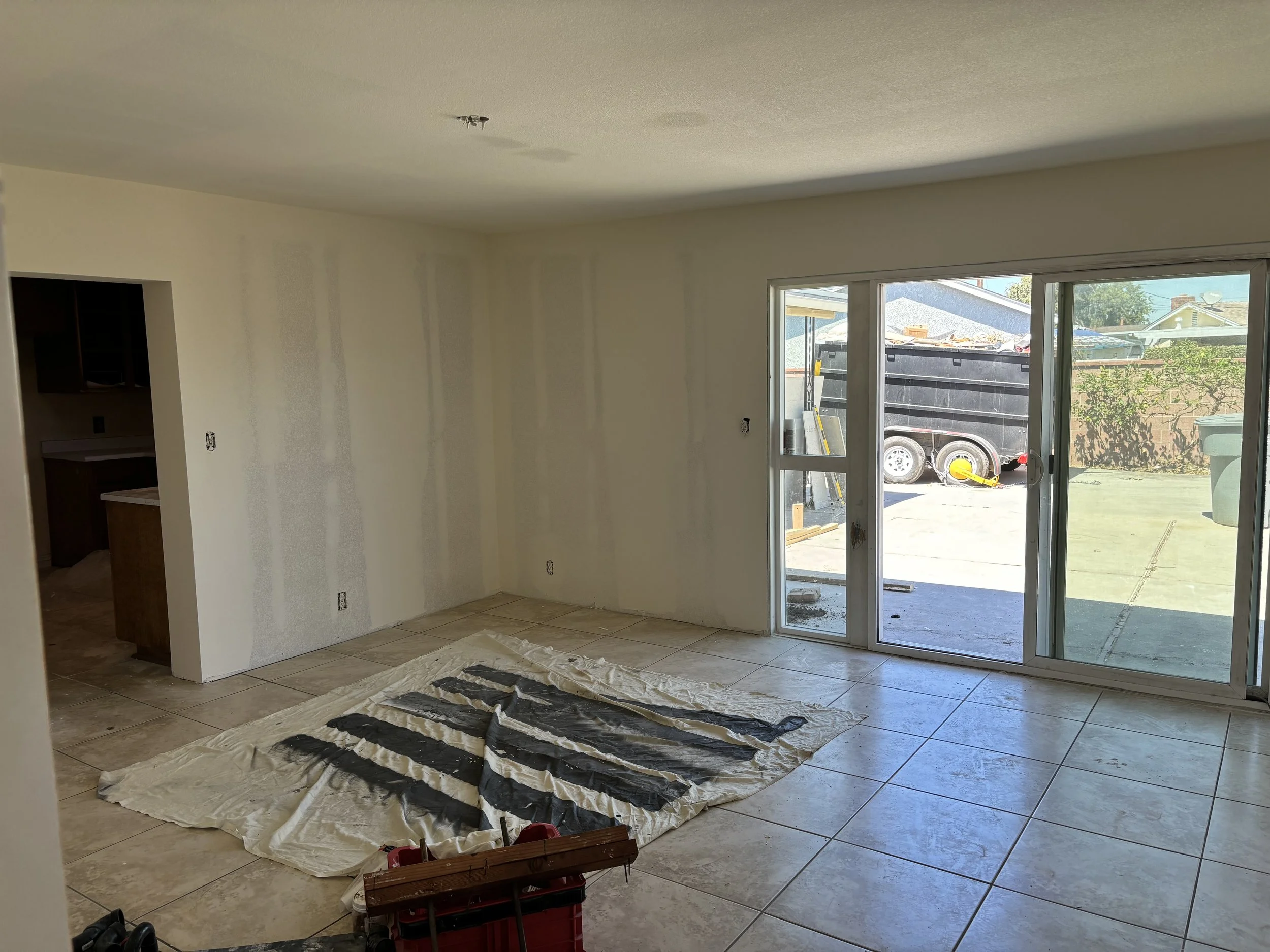 Empty living room with tiled floors, sliding glass door to patio, and unfinished walls with visible drywall seams, under construction.