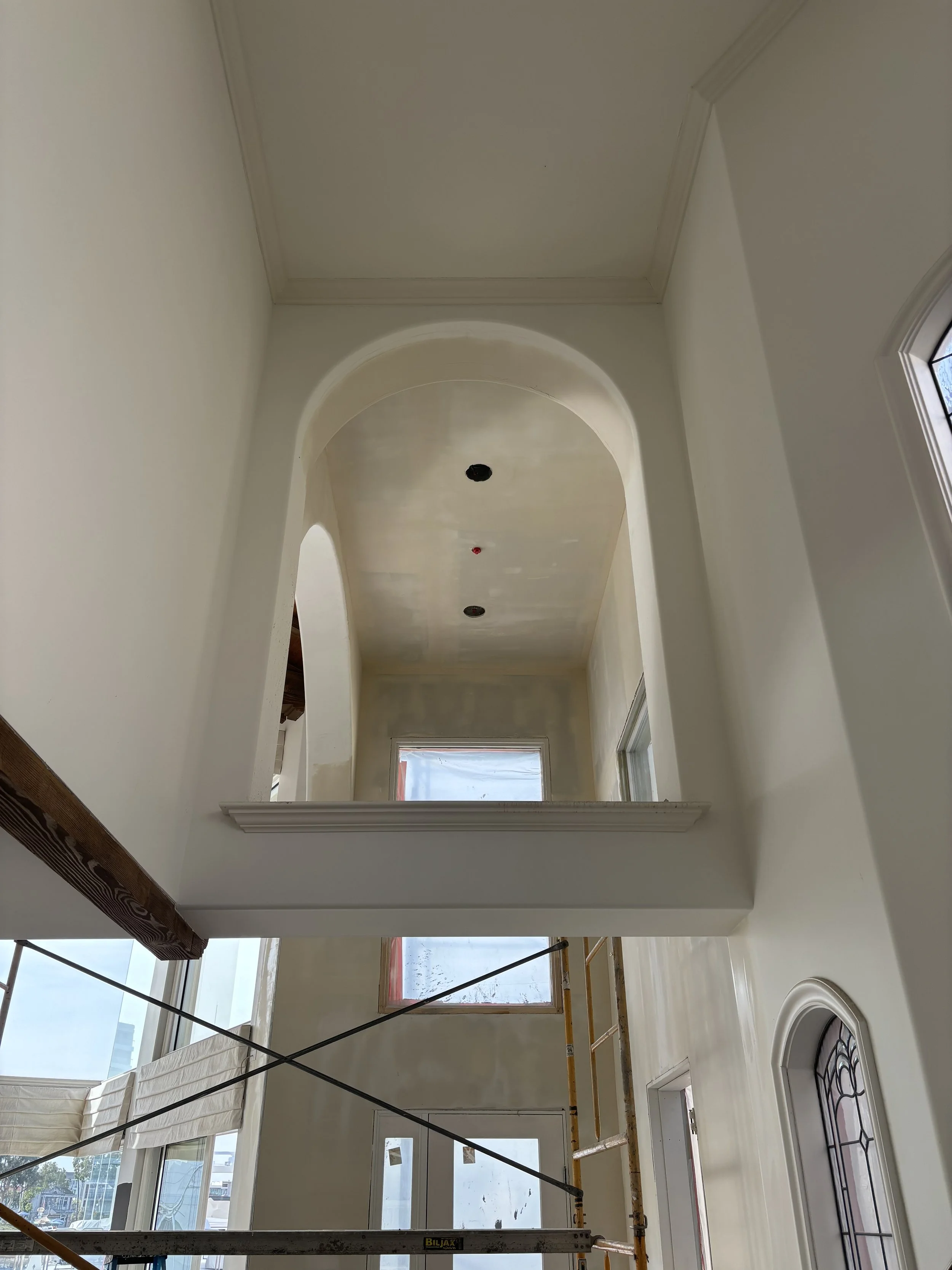 Interior view of a building under construction, showing high ceiling with an arch, windows, and a scaffold.