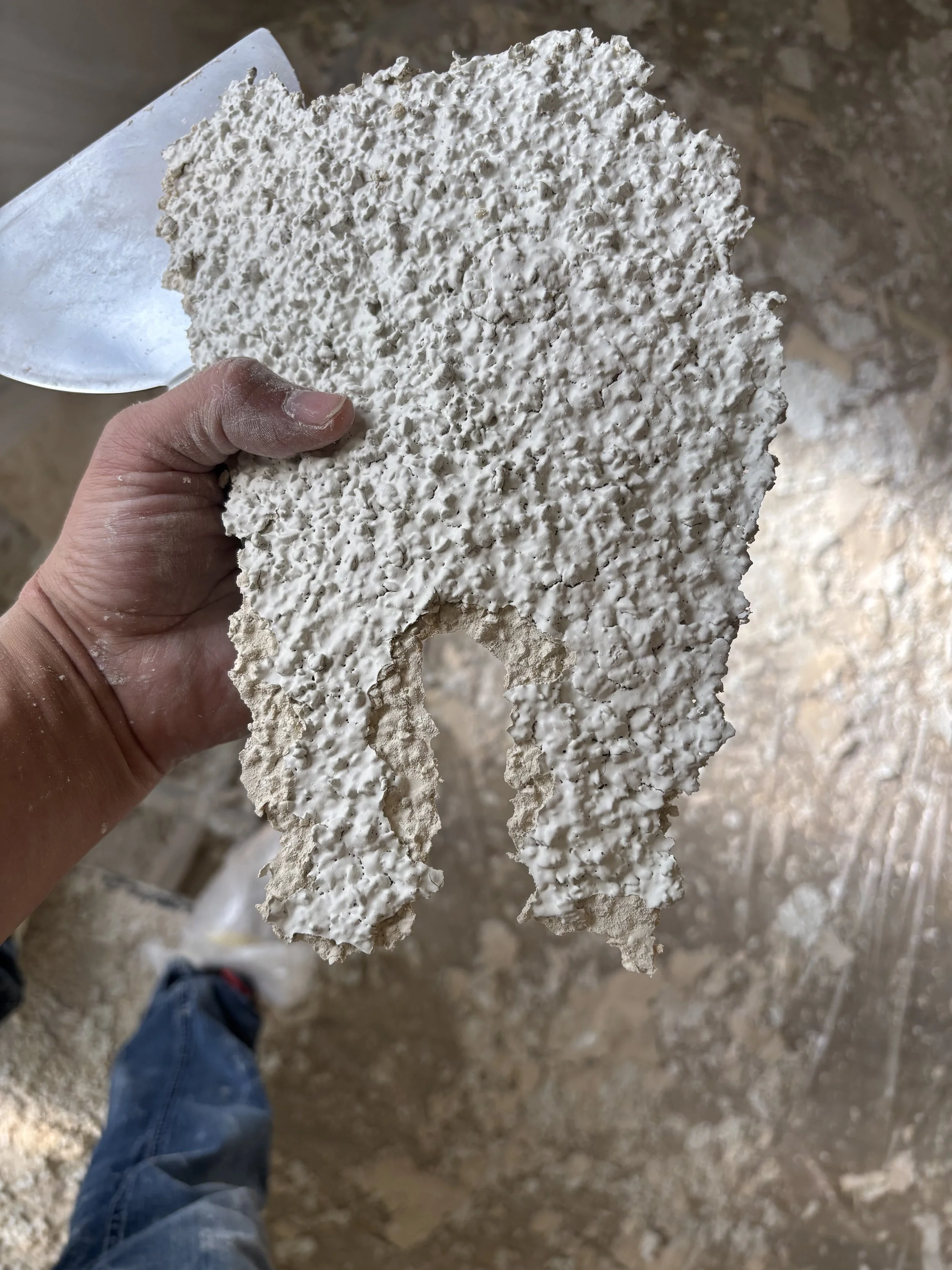 Professional drywaller holding a complex acoustic popcorn ceiling texture sample to ensure a perfect match for a ceiling patch and repair job.