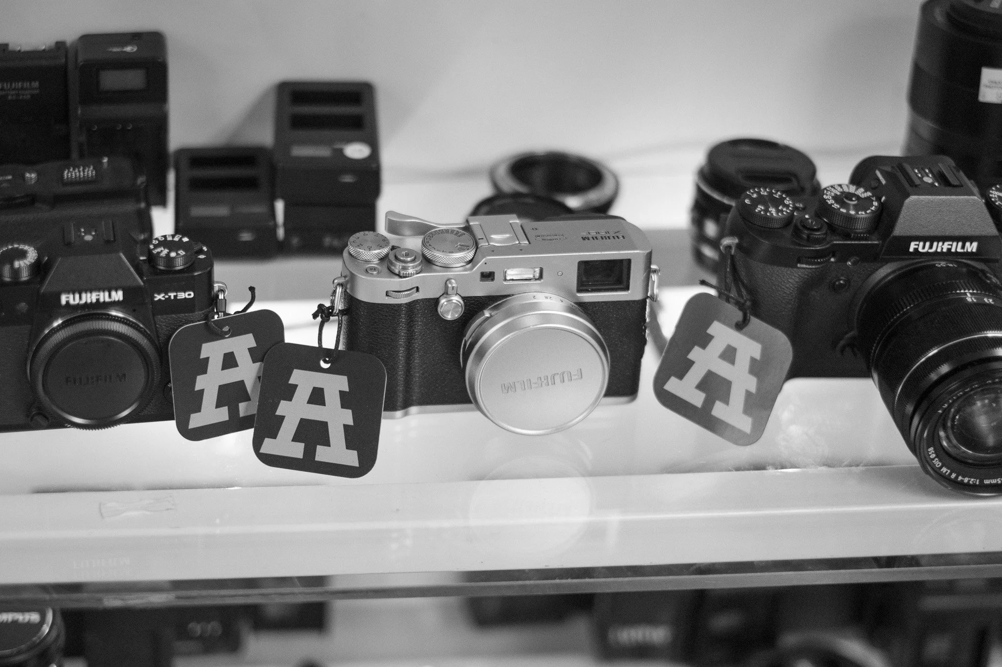A display of three Fujifilm cameras and multiple camera accessories, including lenses and batteries, arranged on a white surface.
