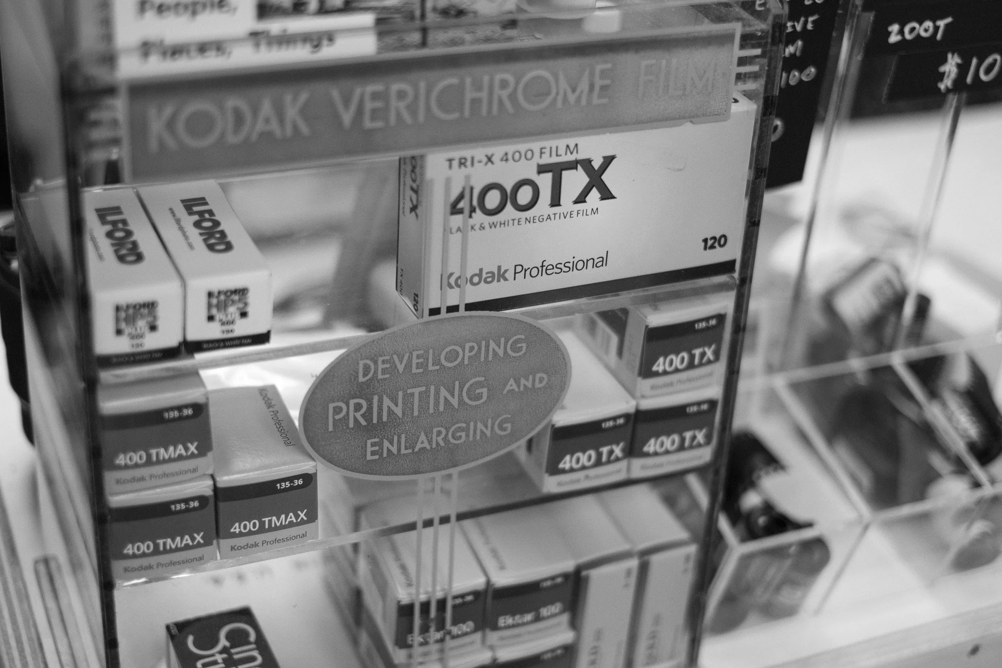 Boxes of Kodak Professional 400 TMAX black and white film on display in a store, with a sign indicating they develop printing and enlarging.