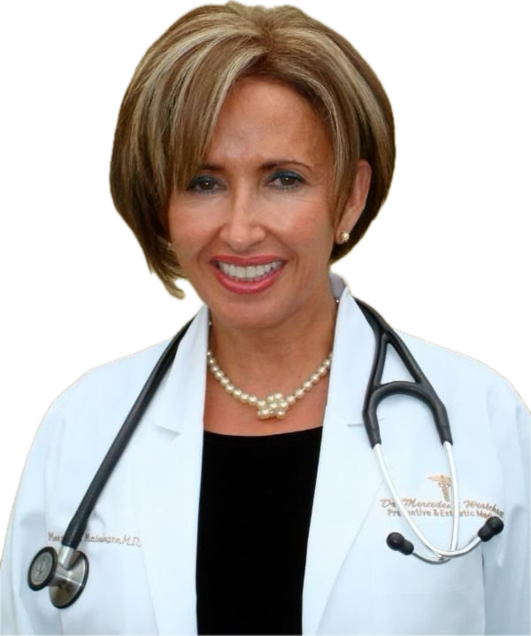 A smiling female doctor with short, blonde hair, wearing a white coat, a stethoscope around her neck, a pearl necklace, and pearl earrings.