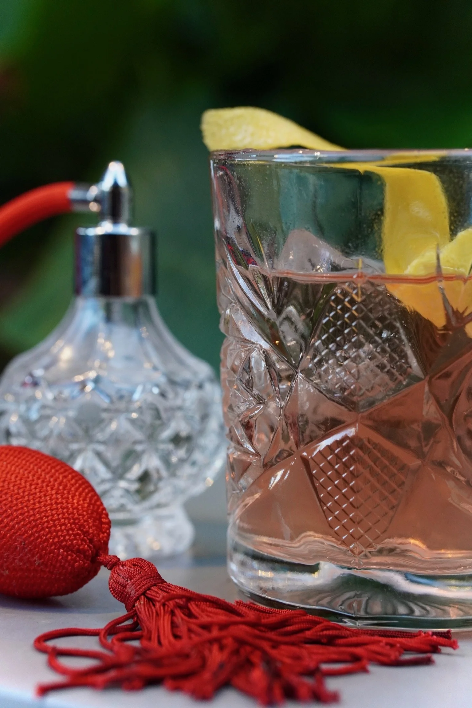 A close-up of a glass of pink-colored drink with lemon slices and ice cubes, with a crystal decanter and a red silk tassel in the background.