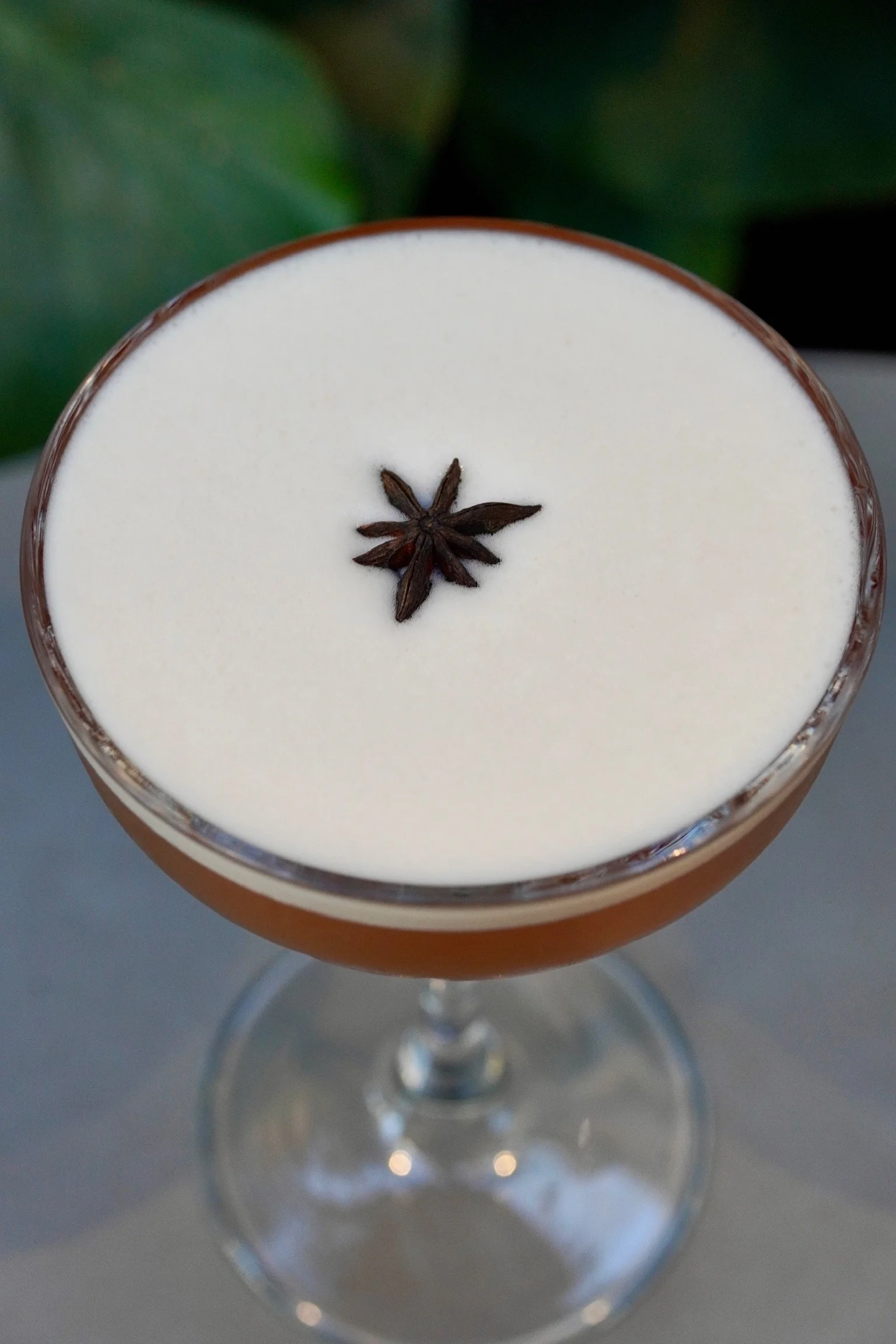A cocktail in a glass with a creamy white foam top garnished with a star anise seed.