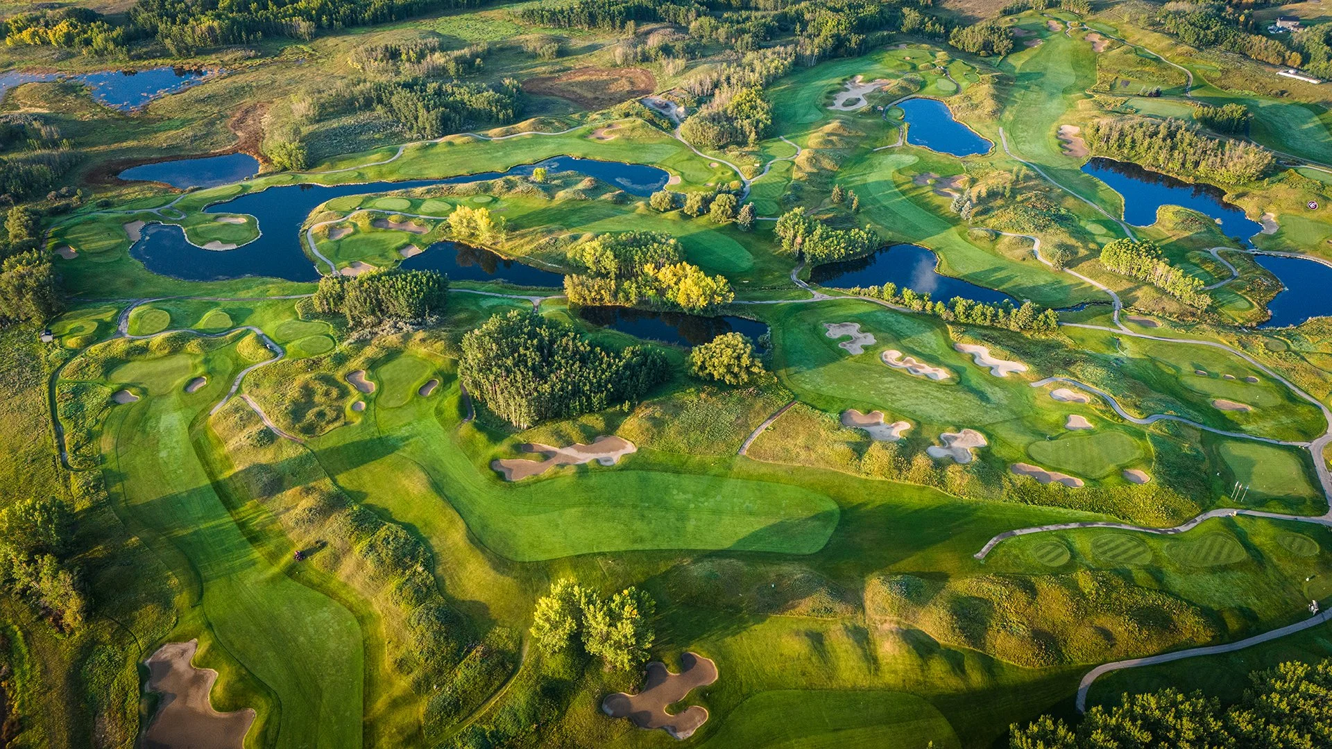 Aerial view of a golf course with lush green fairways, multiple ponds, sand traps, and trees.