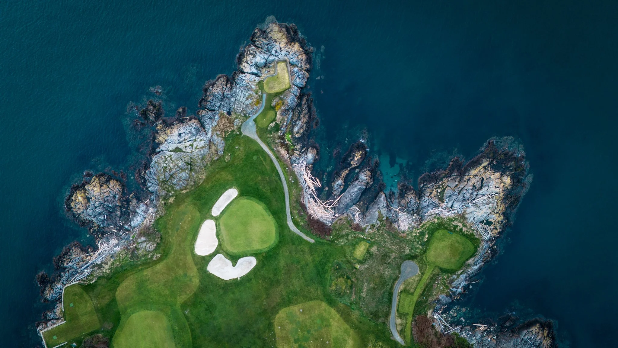 Aerial view of a coastal golf course with green fairways and sandy bunkers, surrounded by rocky cliffs and deep blue ocean.