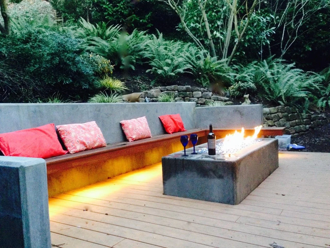 A photo showing a concrete retaining wall with a built-in Ipe bench, custom fire pit and composite deck.
