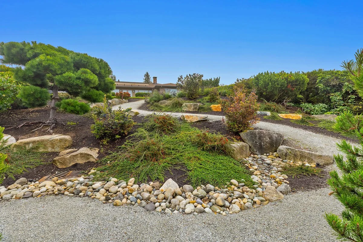 Photograph of a landscaped garden featuring a gravel pathway, various green shrubs, and decorative rocks.