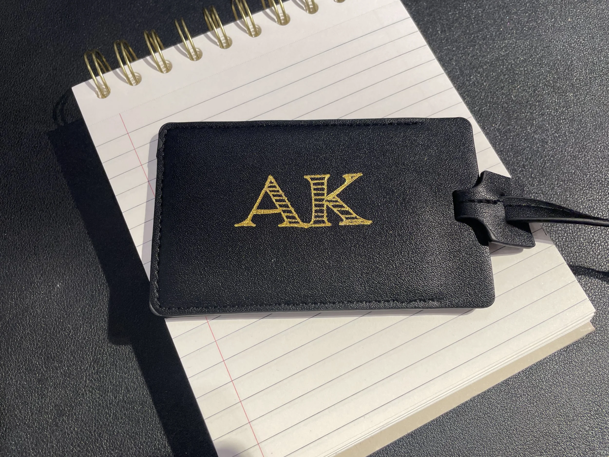 Black Designer Wallet with yellow embroidered initials 'AK' on a lined notebook.