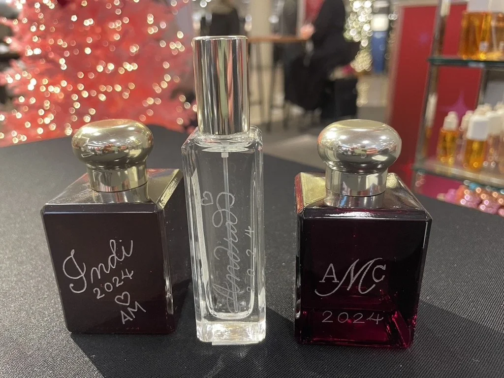 Three perfume bottles with silver caps placed on a dark surface, with a festive, blurred background.