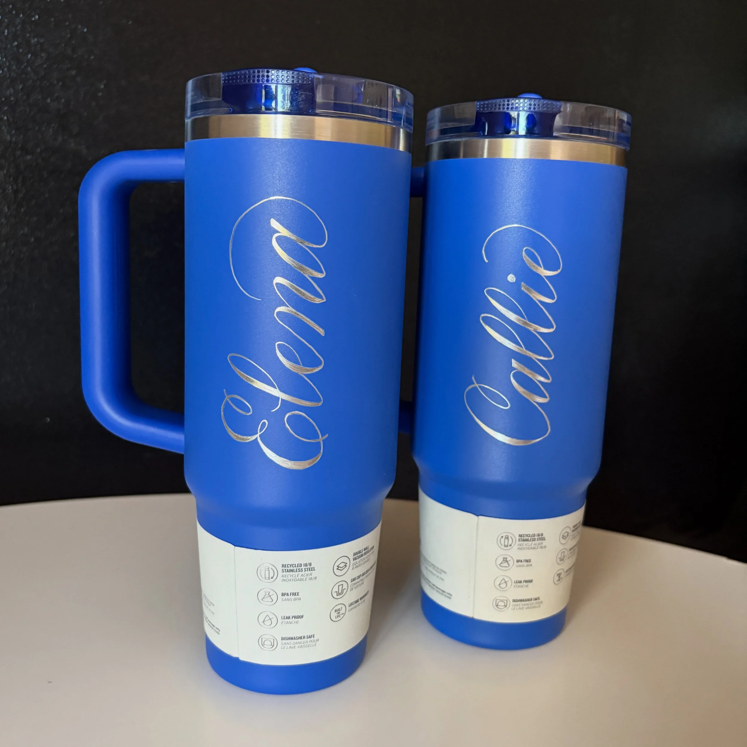Two blue travel mugs with silver accents and clear lids, featuring the word 'Caldillo' written in cursive on the front.