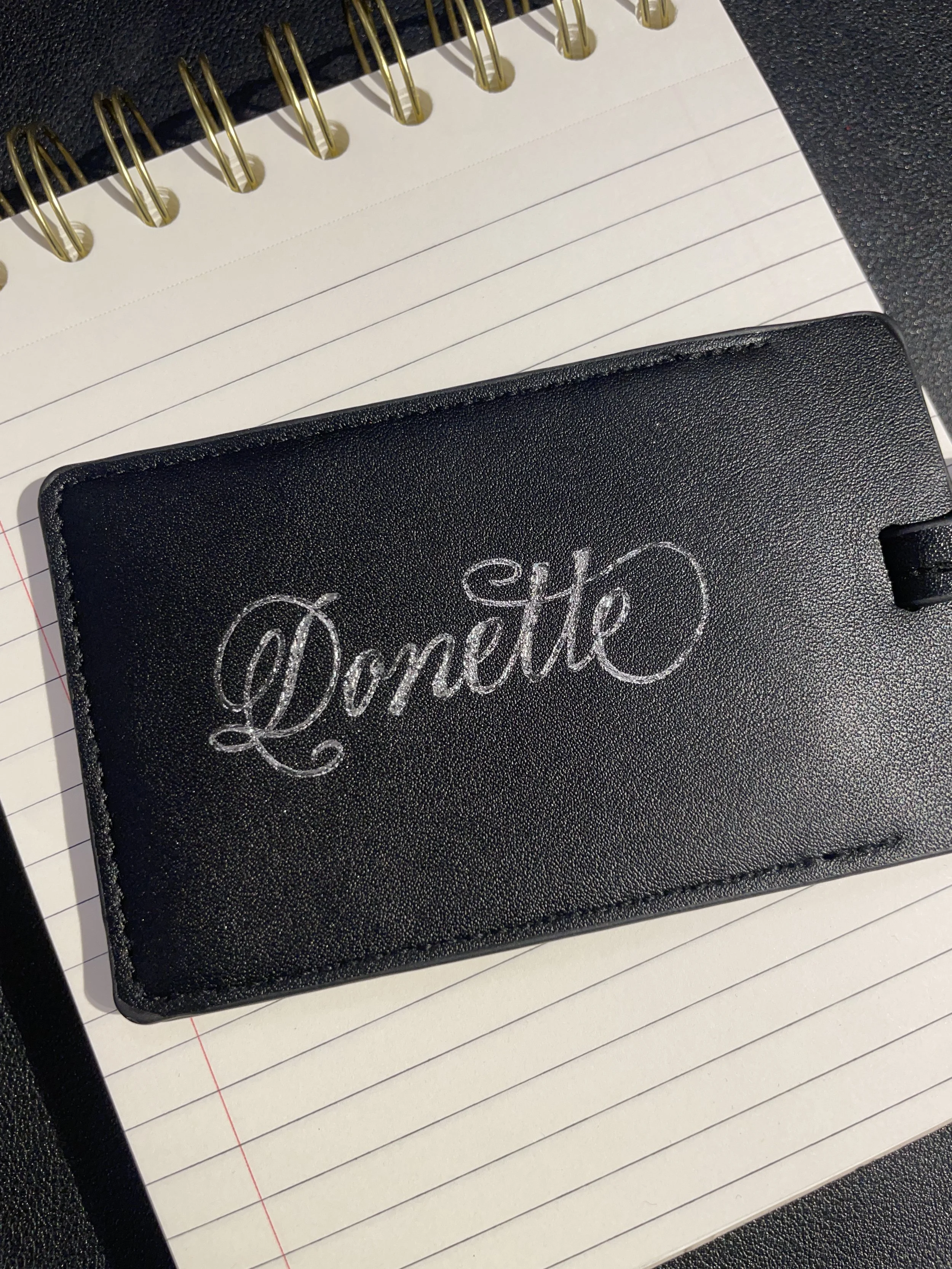 A black leather wallet with the word 'Love' embroidered in white cursive on the front, resting on a lined notepad.